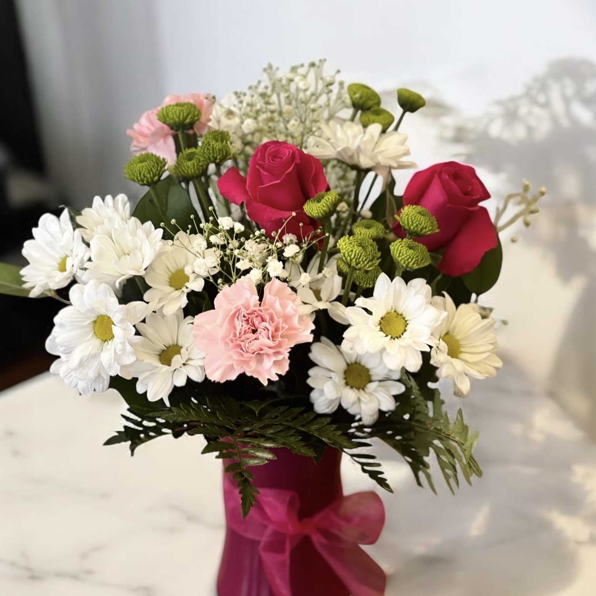 Bouquet of pink roses, white daisies, and a pink carnation in a magenta vase