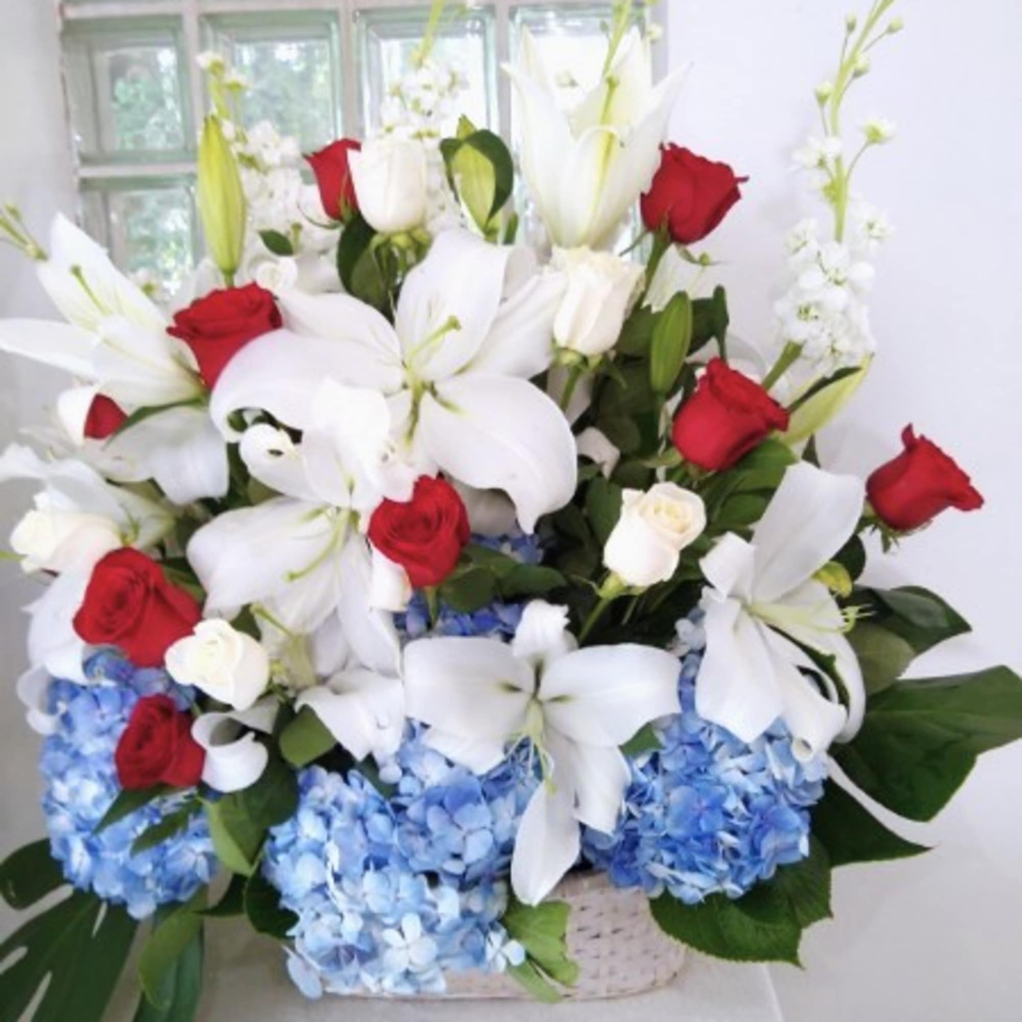 Arrangement of red roses, white lilies, and blue hydrangeas in a basket