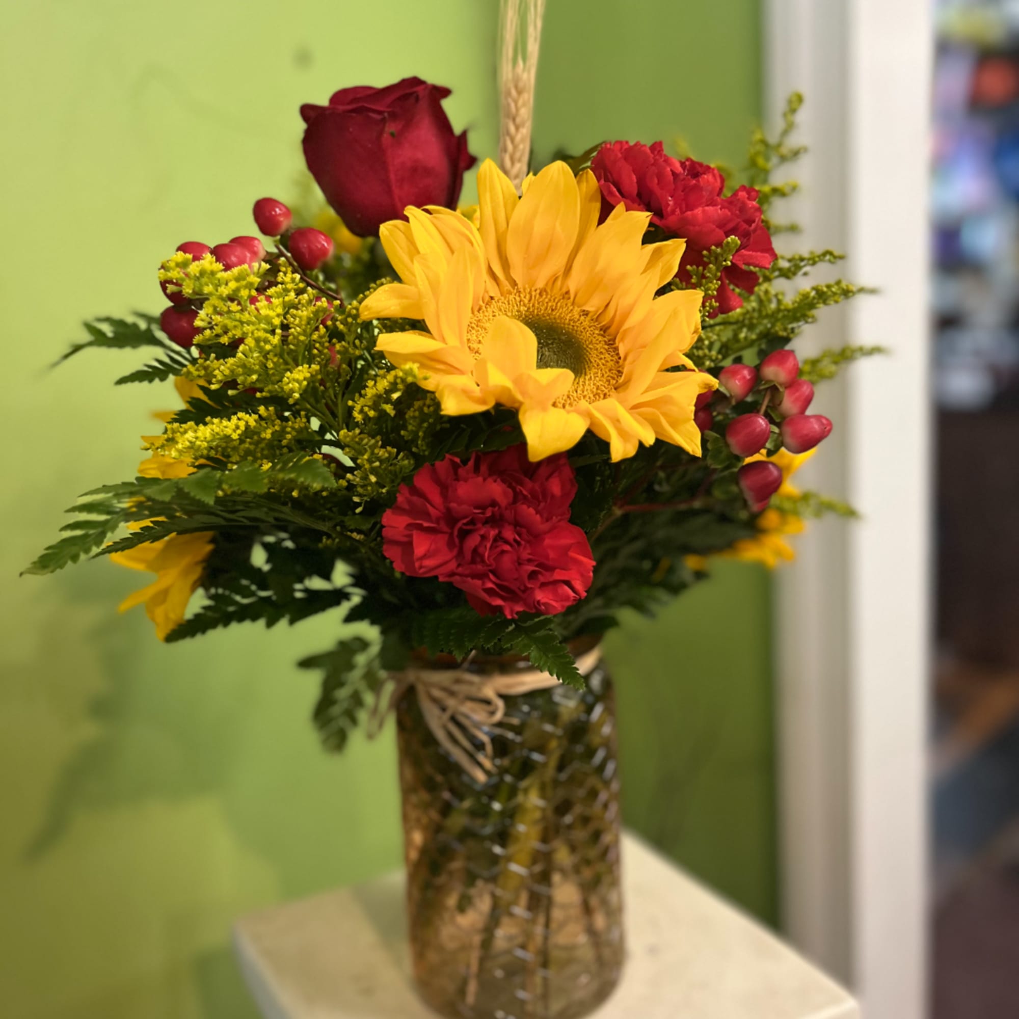 Bouquet of sunflowers, red roses, and carnations in a glass vase