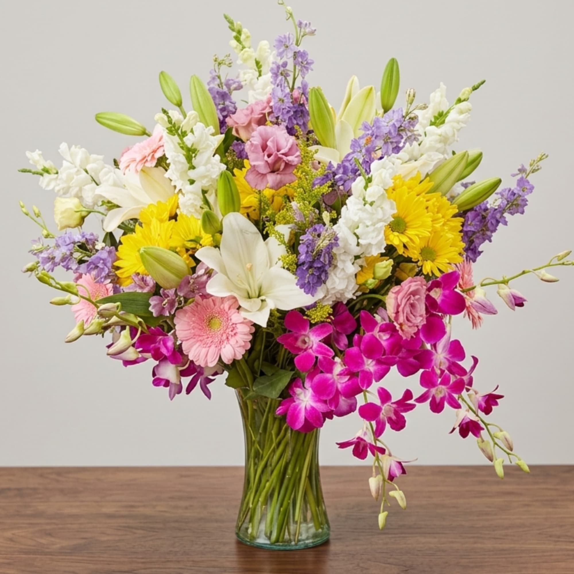 Mixed bouquet of lilies, orchids, daisies, and purple blooms in a glass vase