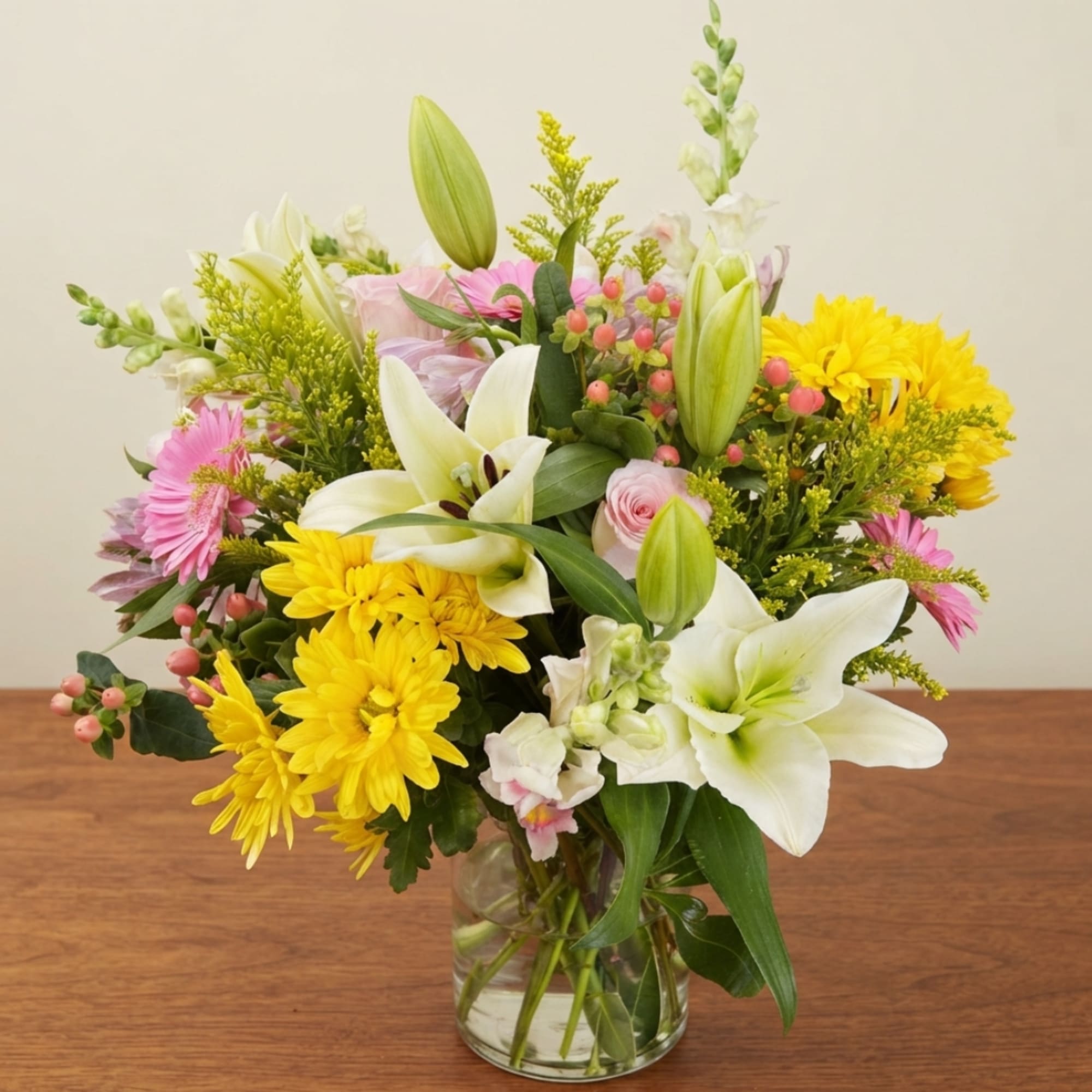 Mixed bouquet of white lilies, yellow daisies, and pink flowers in a glass vase