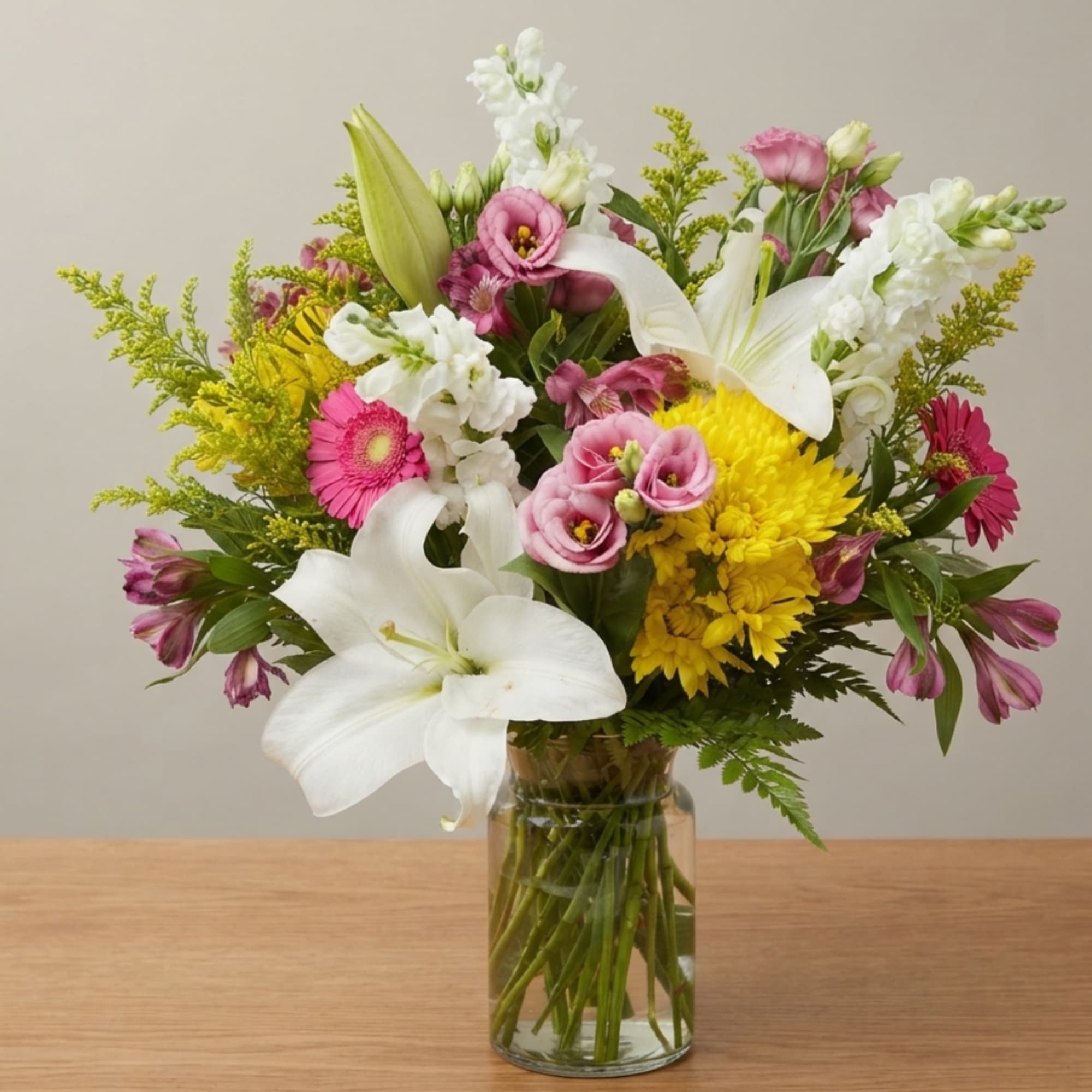 Mixed bouquet of white lilies, pink blooms, and yellow flowers in a glass vase