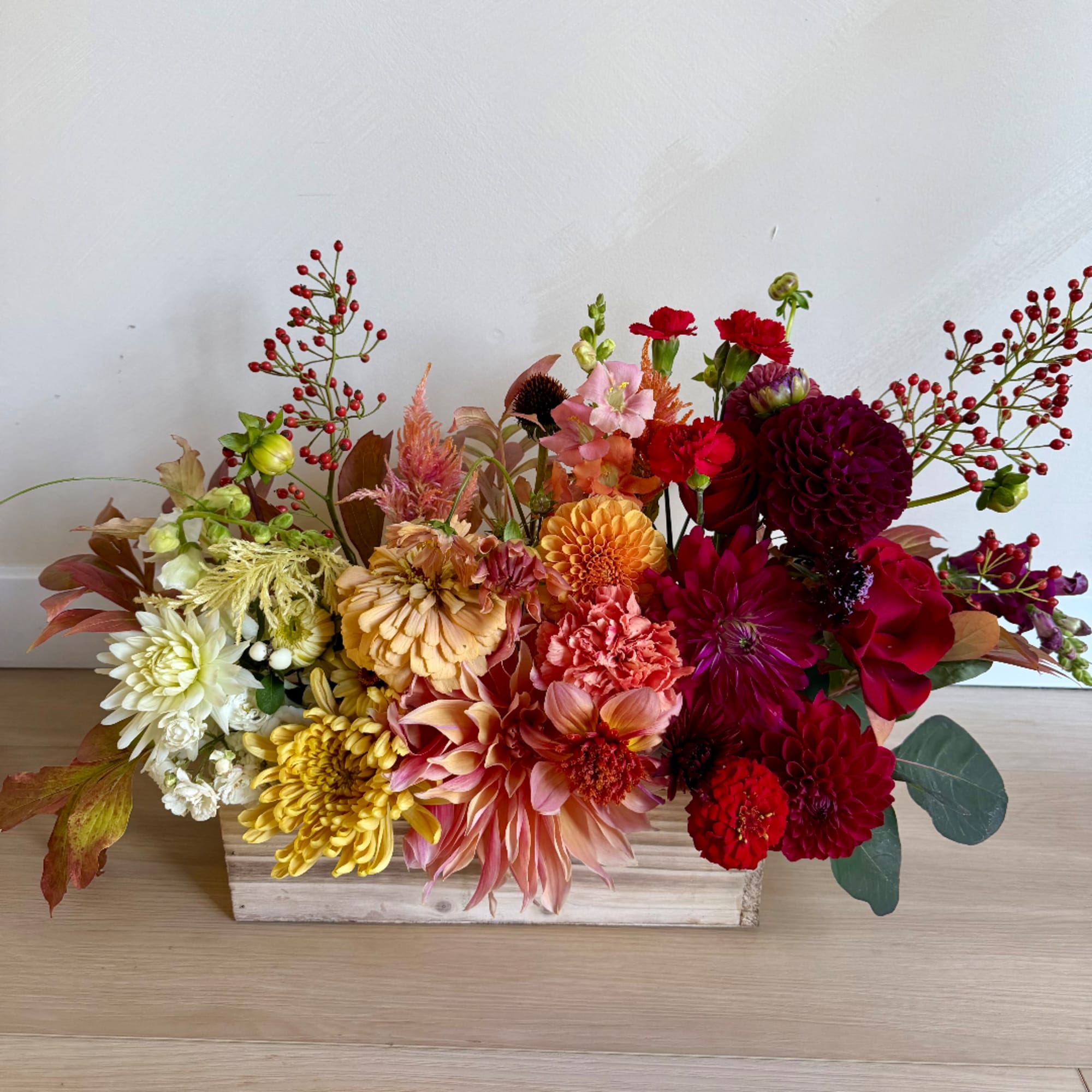 Mixed floral arrangement in a wooden box with red, pink, yellow, and white blooms