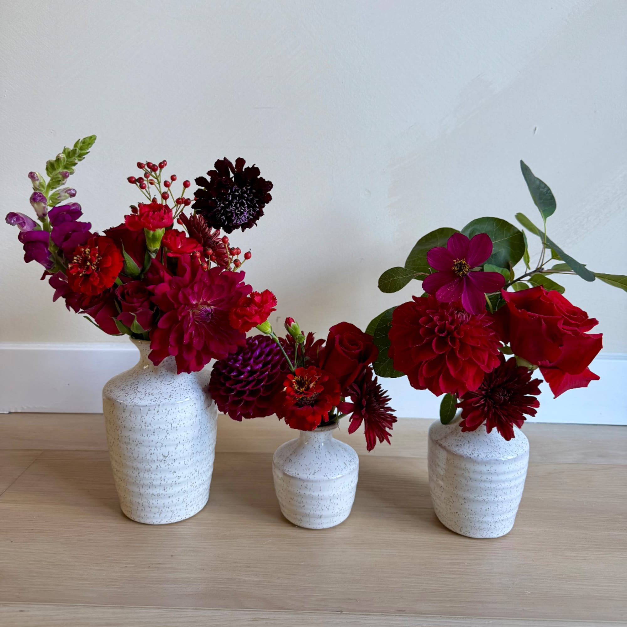 Three red and magenta flower arrangements in white ceramic vases