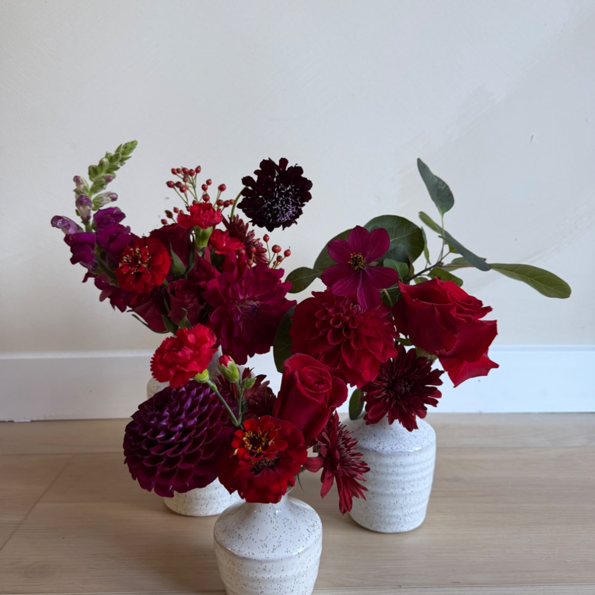 Three red and burgundy floral arrangements in small white vases