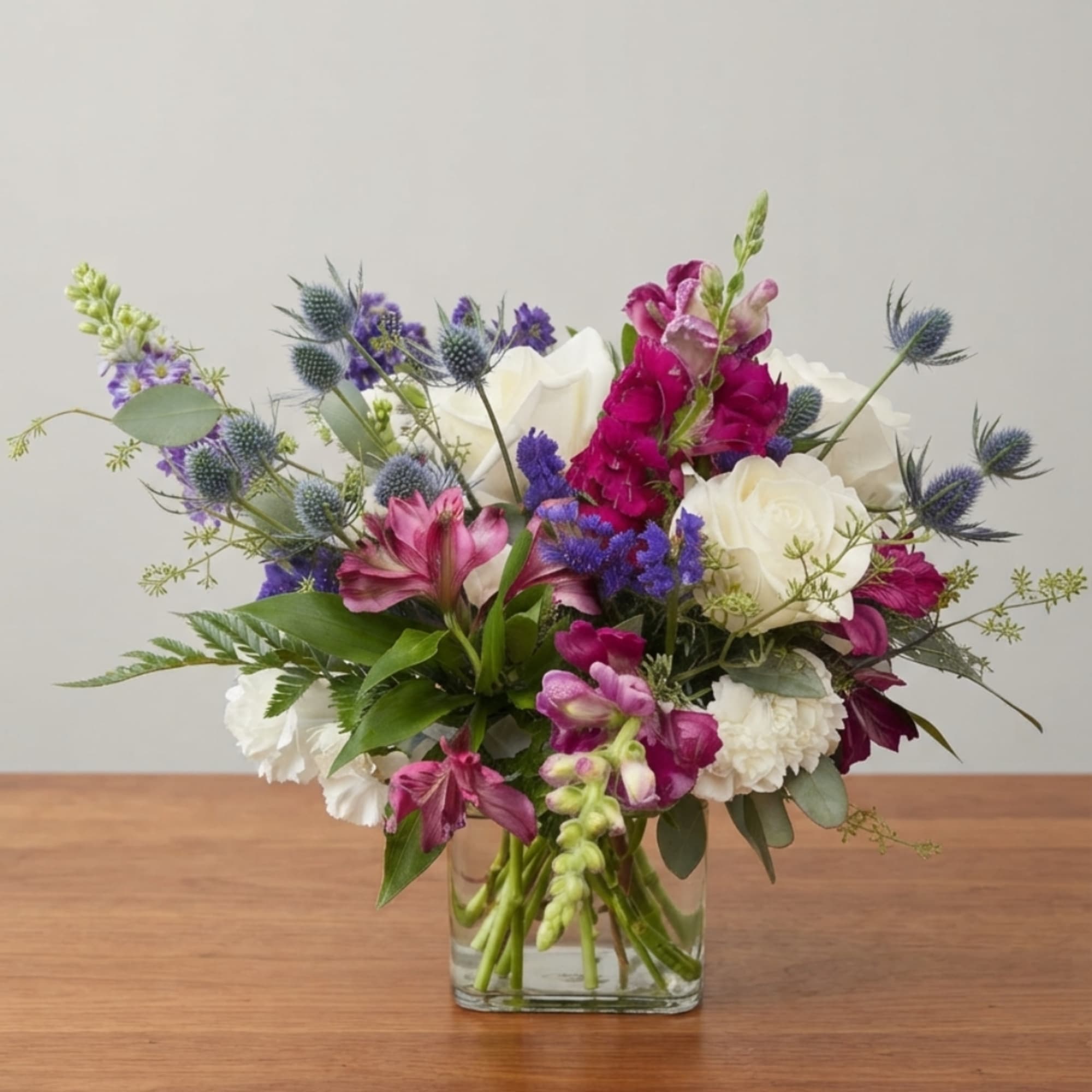 Mixed bouquet of white roses, purple flowers, and pink blooms in a clear glass vase