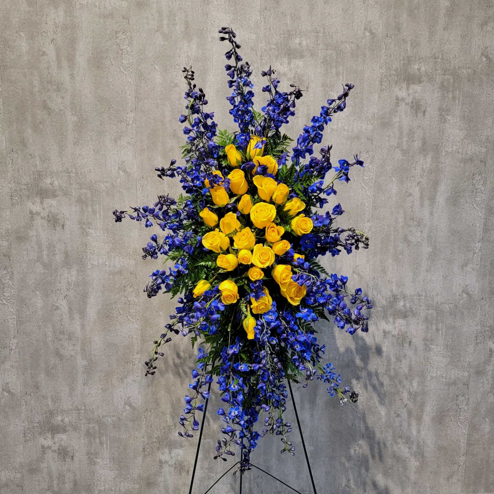 Tall standing arrangement of yellow roses and blue flowers on a black easel