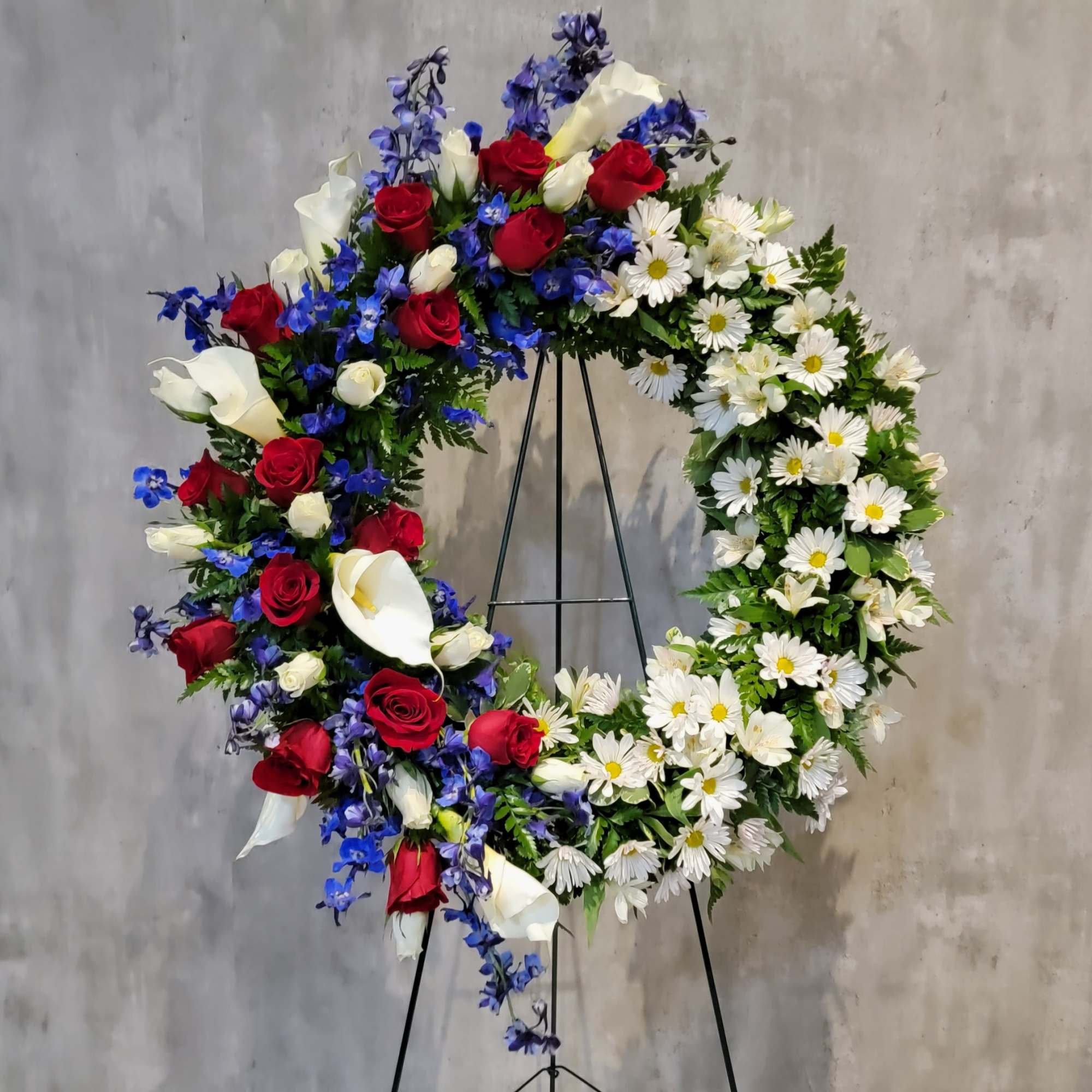 Large floral wreath with red roses, white calla lilies, and white daisies on a stand