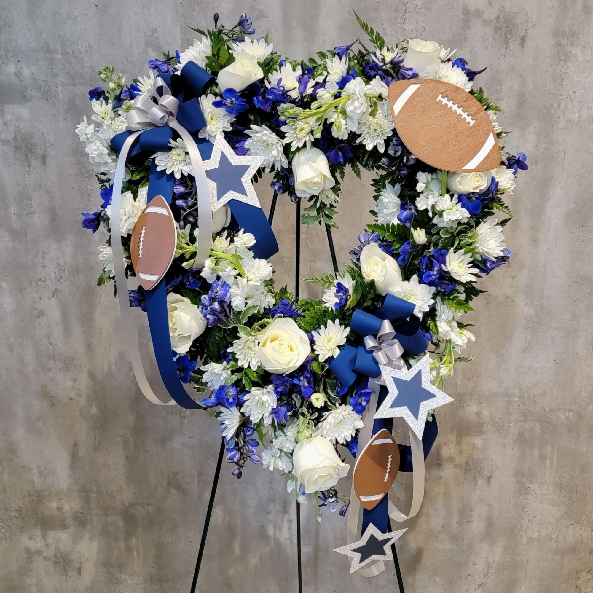 Heart-shaped floral wreath with blue ribbons, stars, and football accents