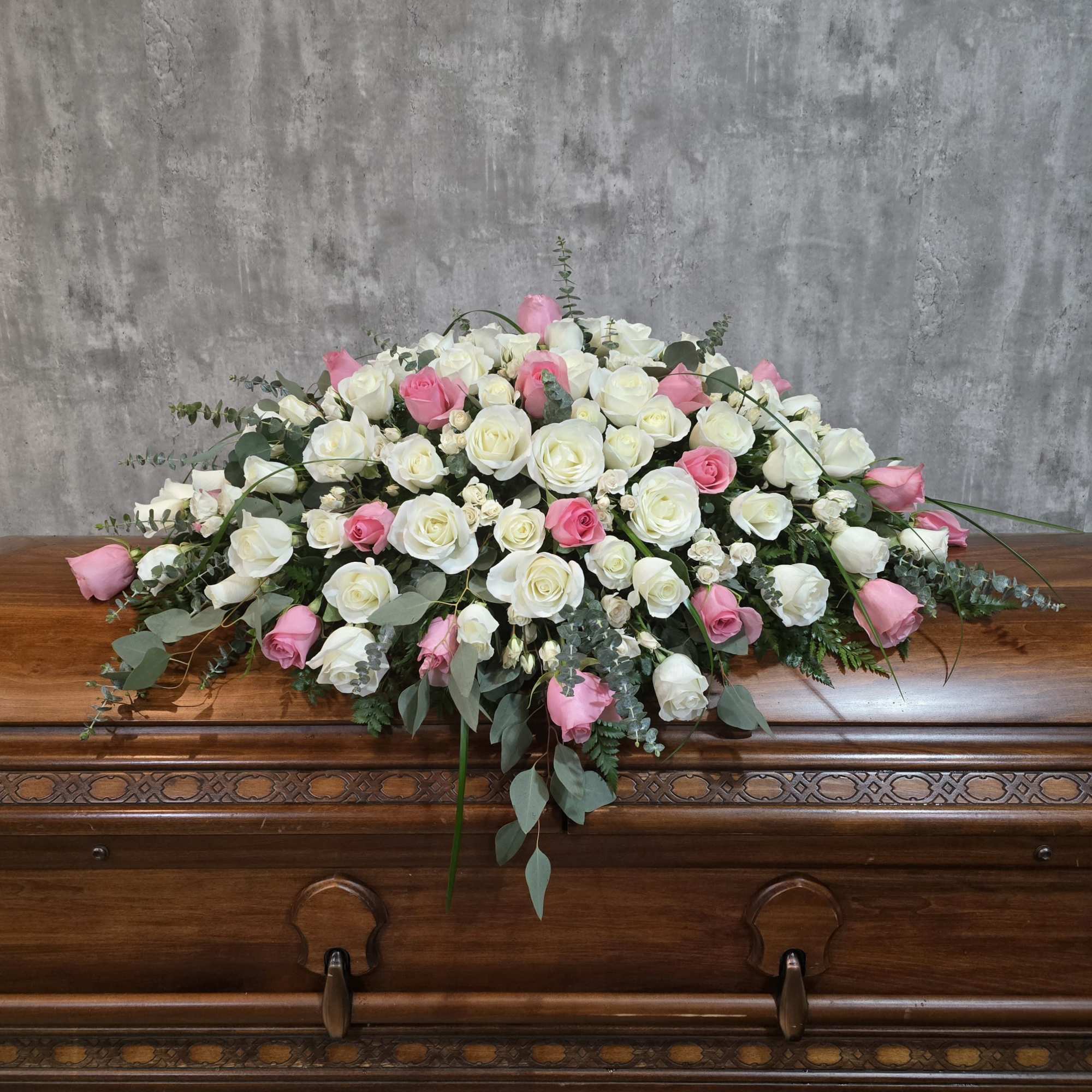White and pink rose casket spray on a wooden casket