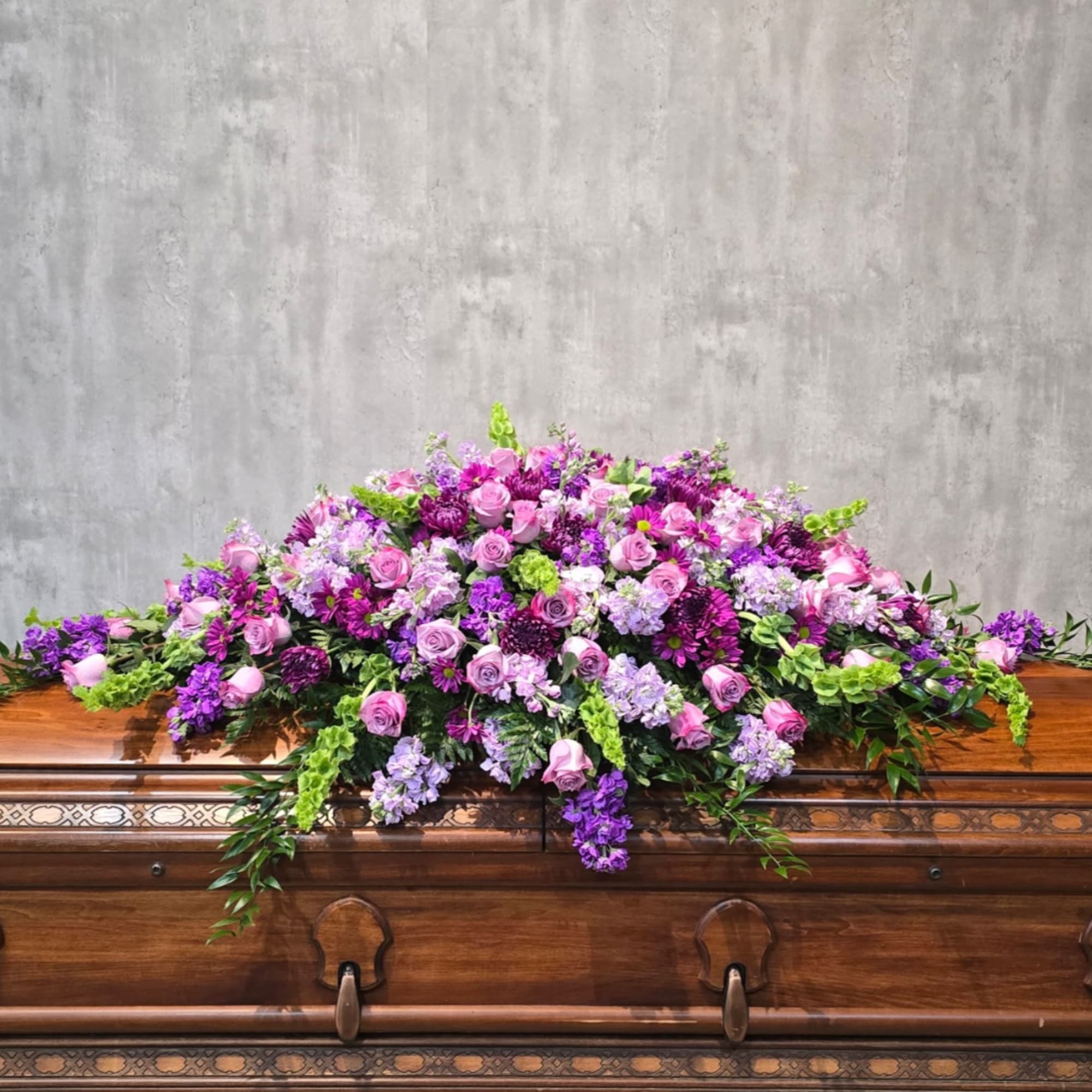 Large pink and purple floral spray arranged on a wooden casket