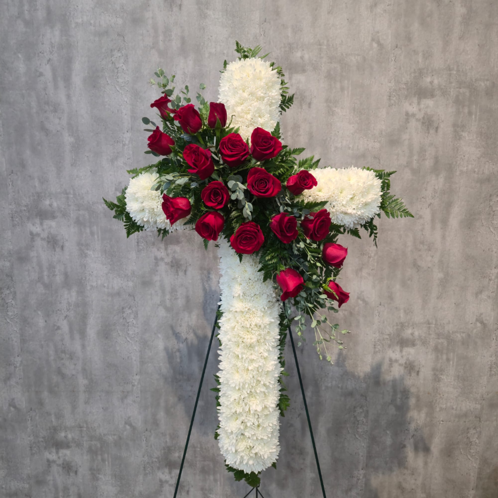 White floral cross with red roses on a stand