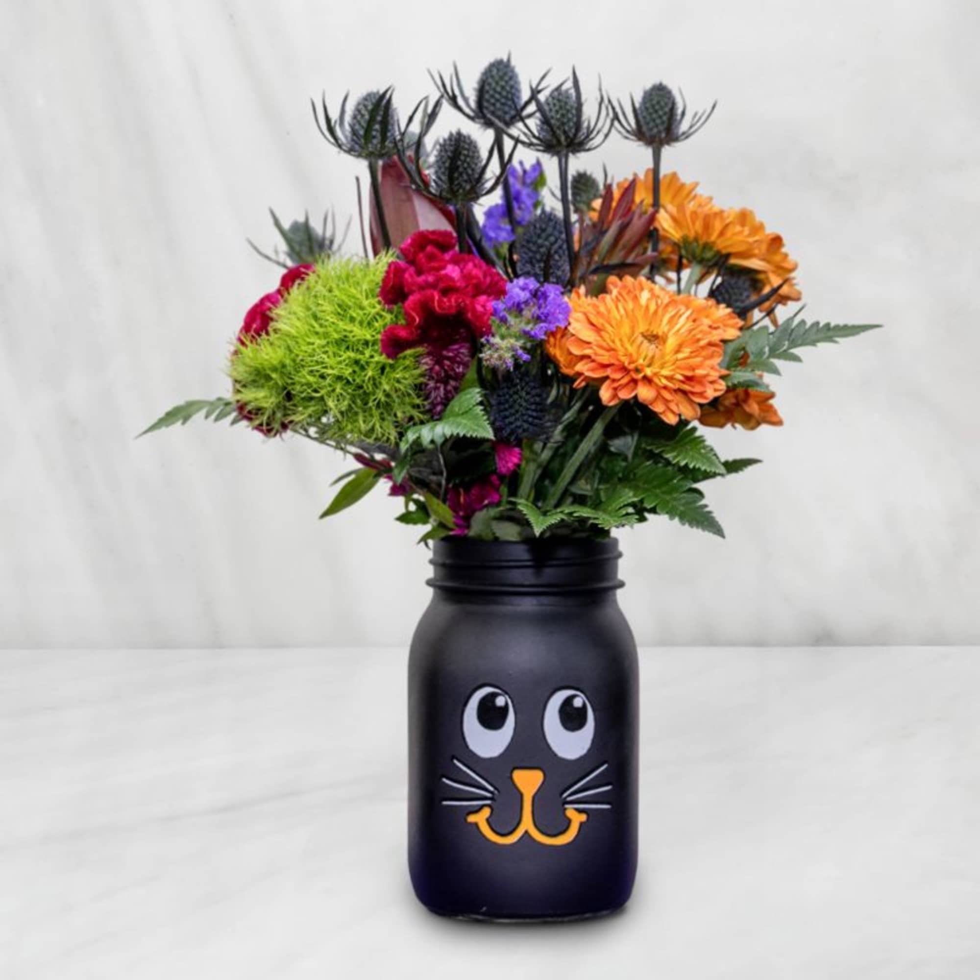 Colorful bouquet in a black jar with a cat face design