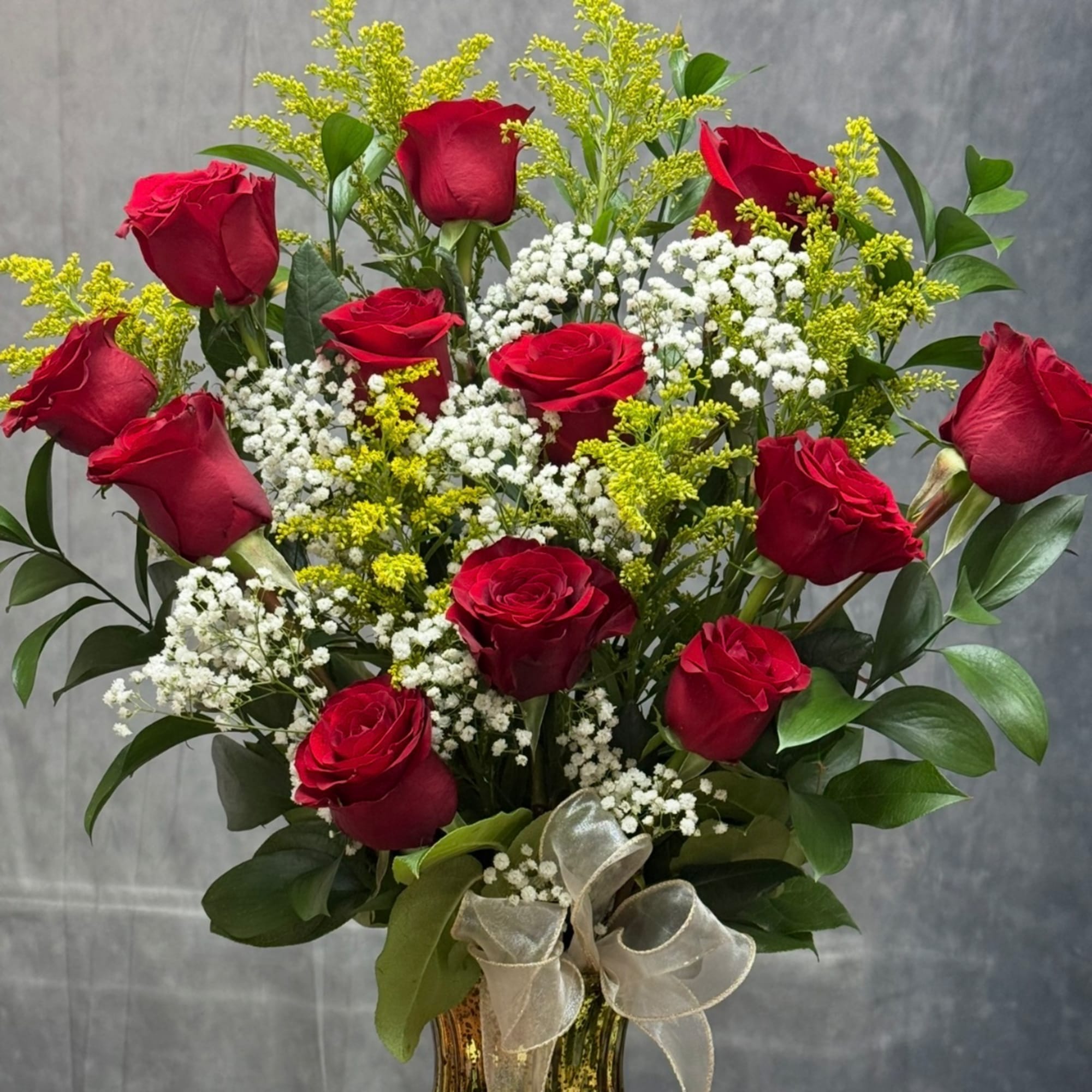 Red roses with white baby's breath in a glass vase with a ribbon