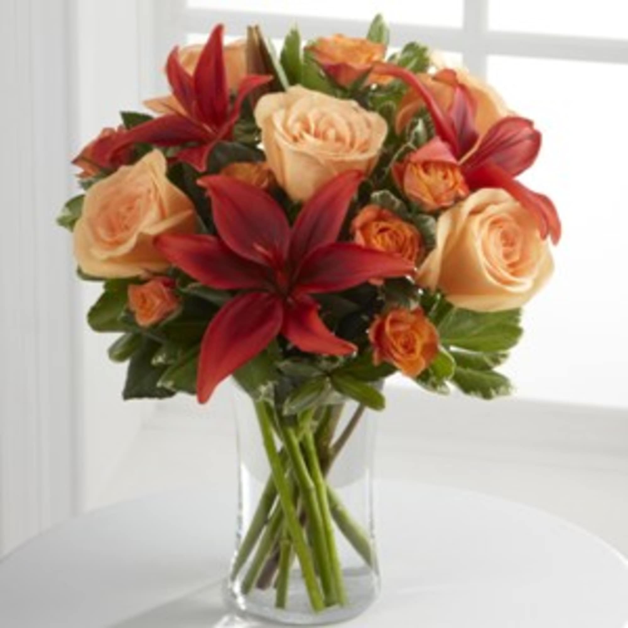 Bouquet of peach roses and red lilies in a clear glass vase