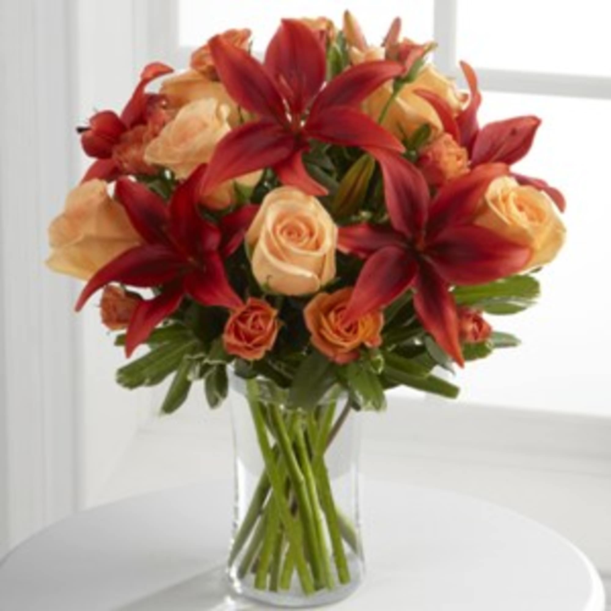 Red lilies and peach roses arranged in a clear glass vase