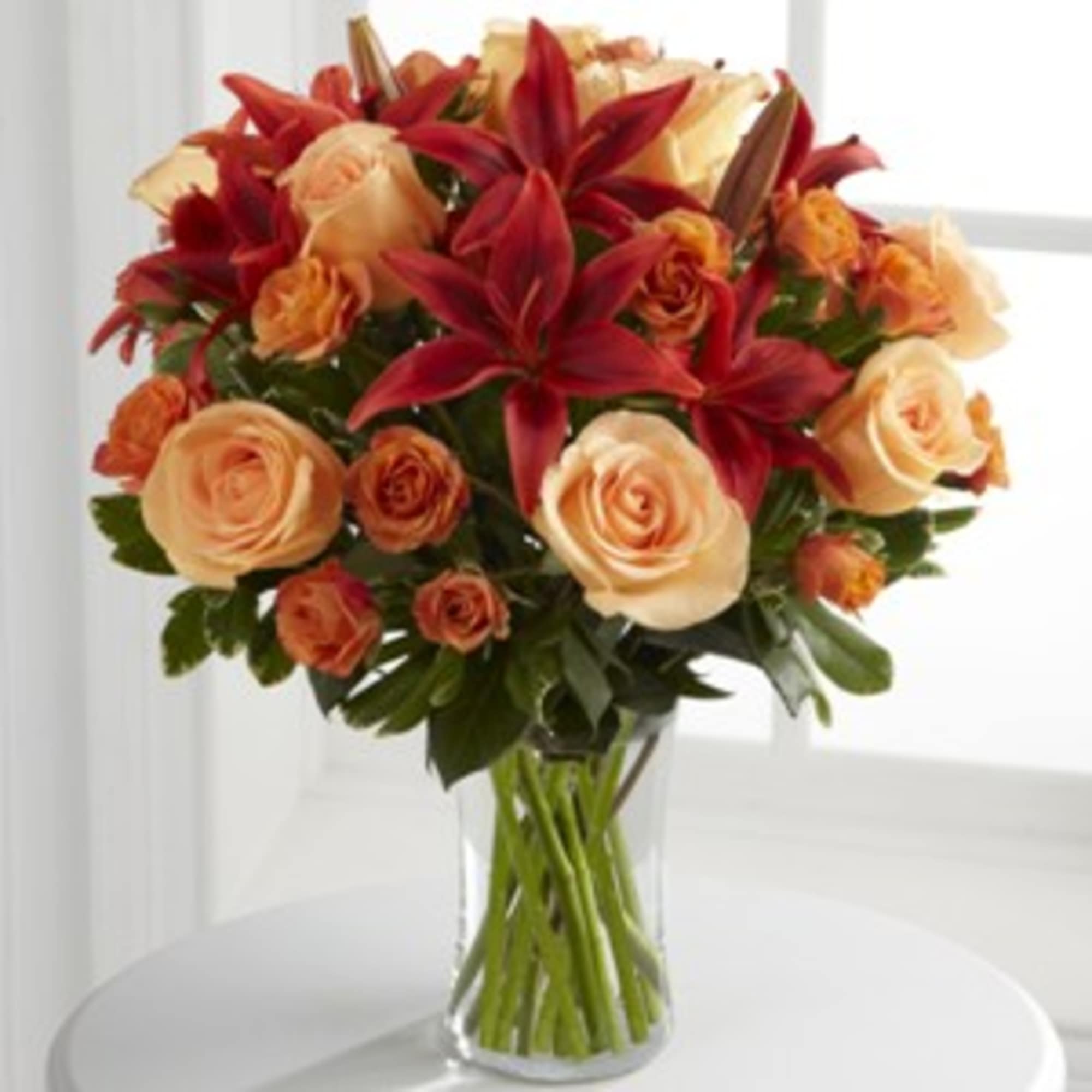 Bouquet of red lilies and peach roses in a clear glass vase