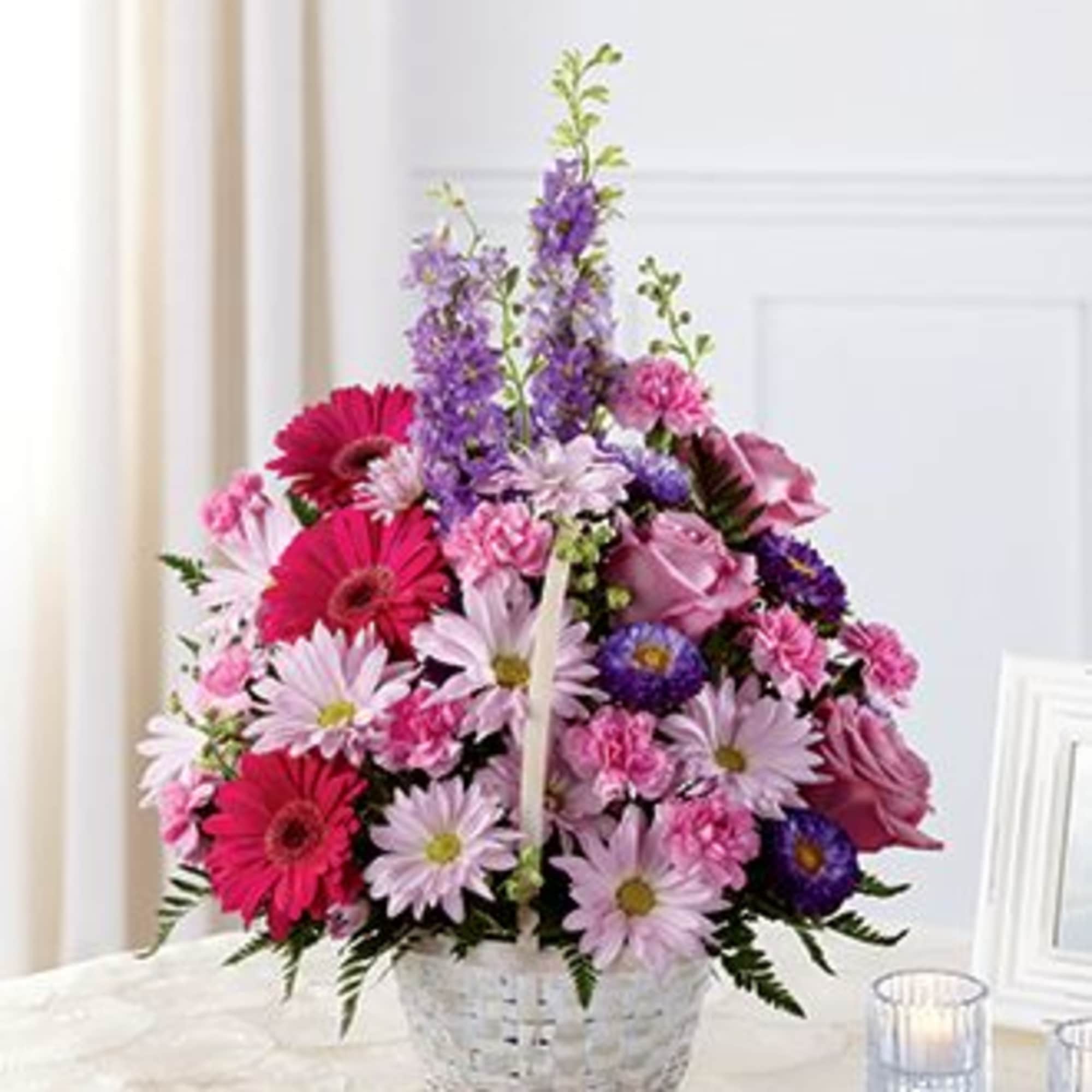 Pink and purple mixed flower basket arrangement in a white woven basket on a table