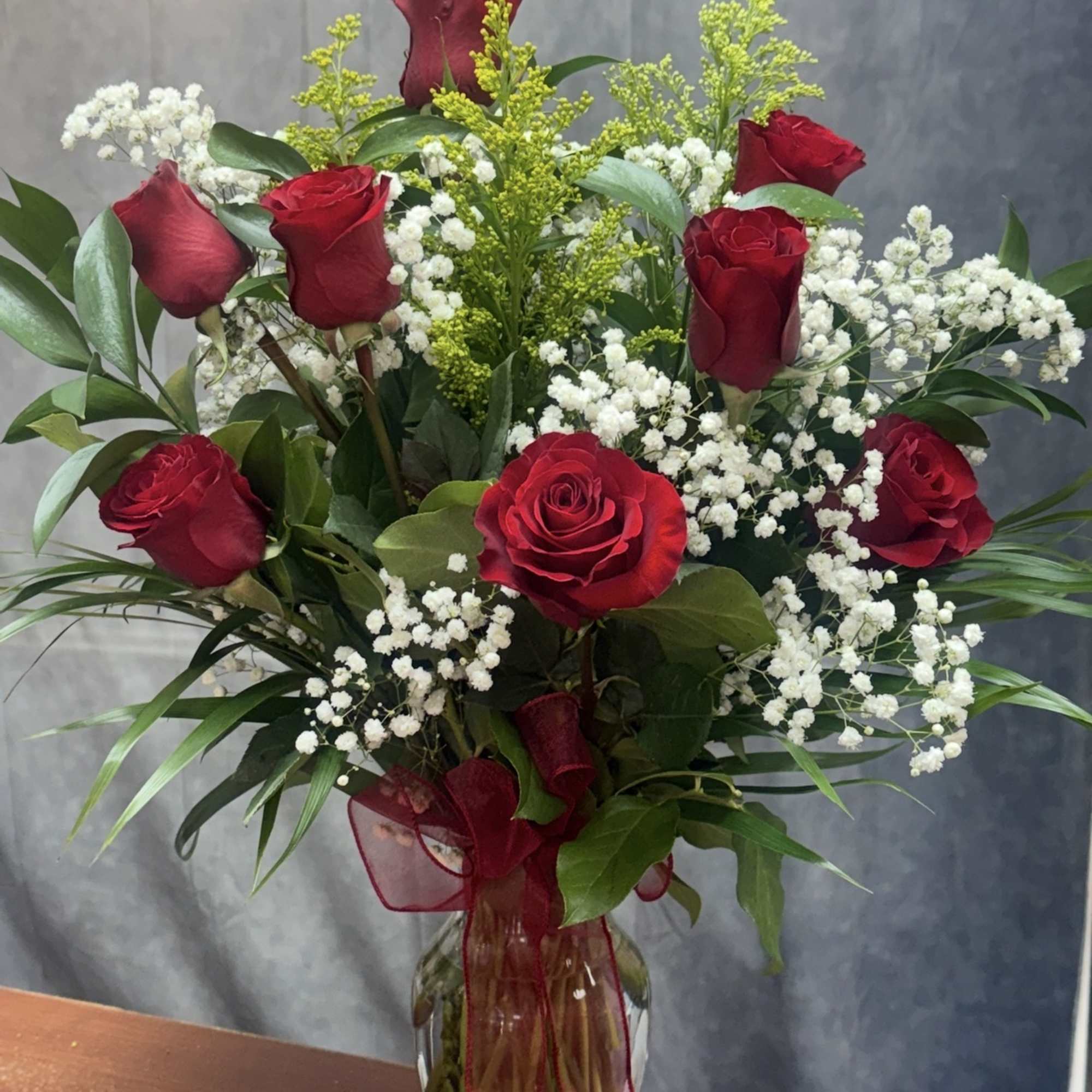 Red roses and white baby's breath in a clear glass vase with a red ribbon