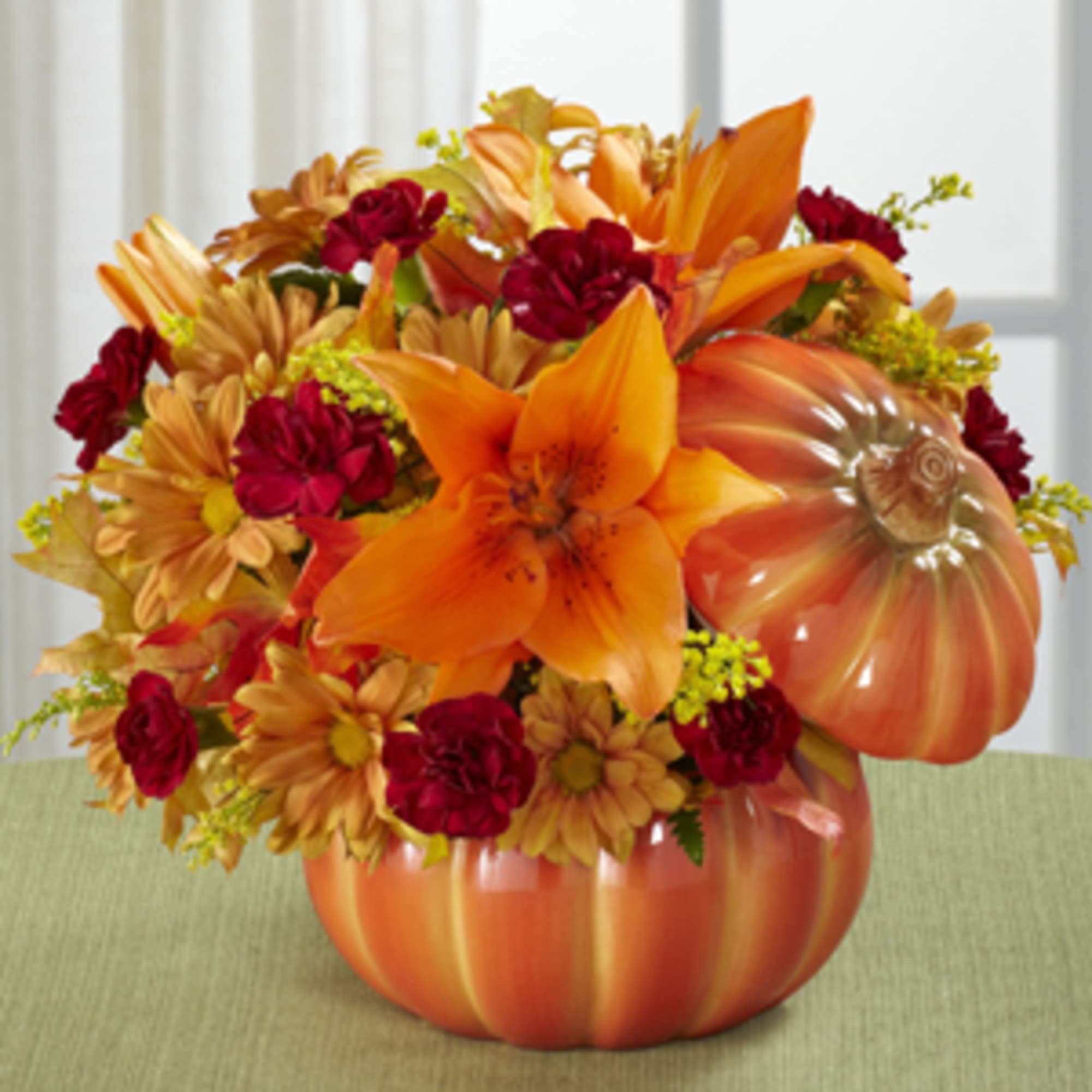 Orange and red floral arrangement in a pumpkin-shaped container