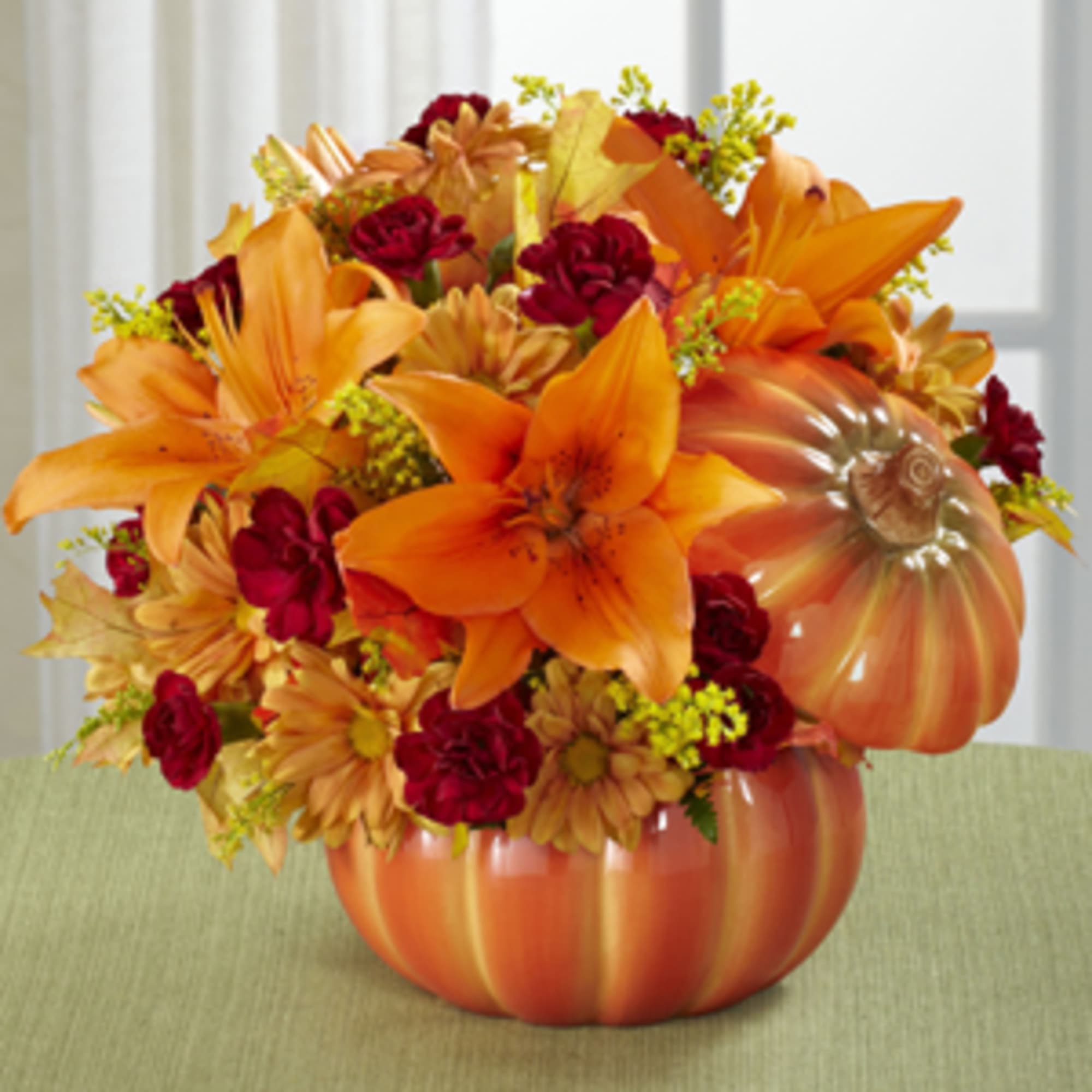 Orange and red floral arrangement in a pumpkin-shaped container