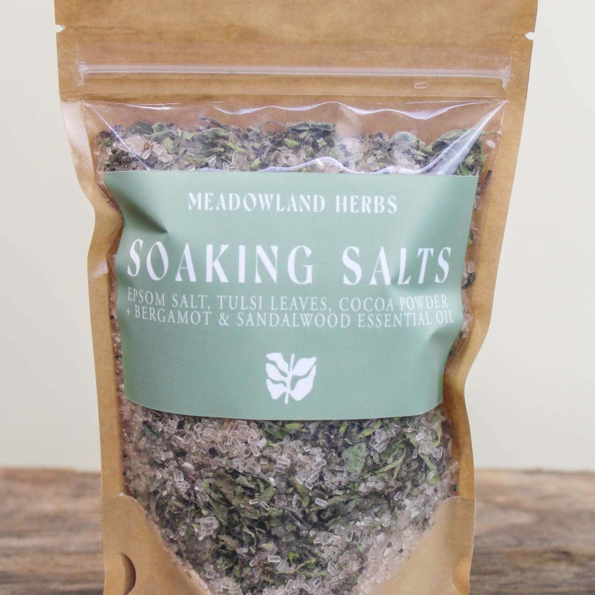A pouch of herbal soaking salts with a green label on a wooden surface