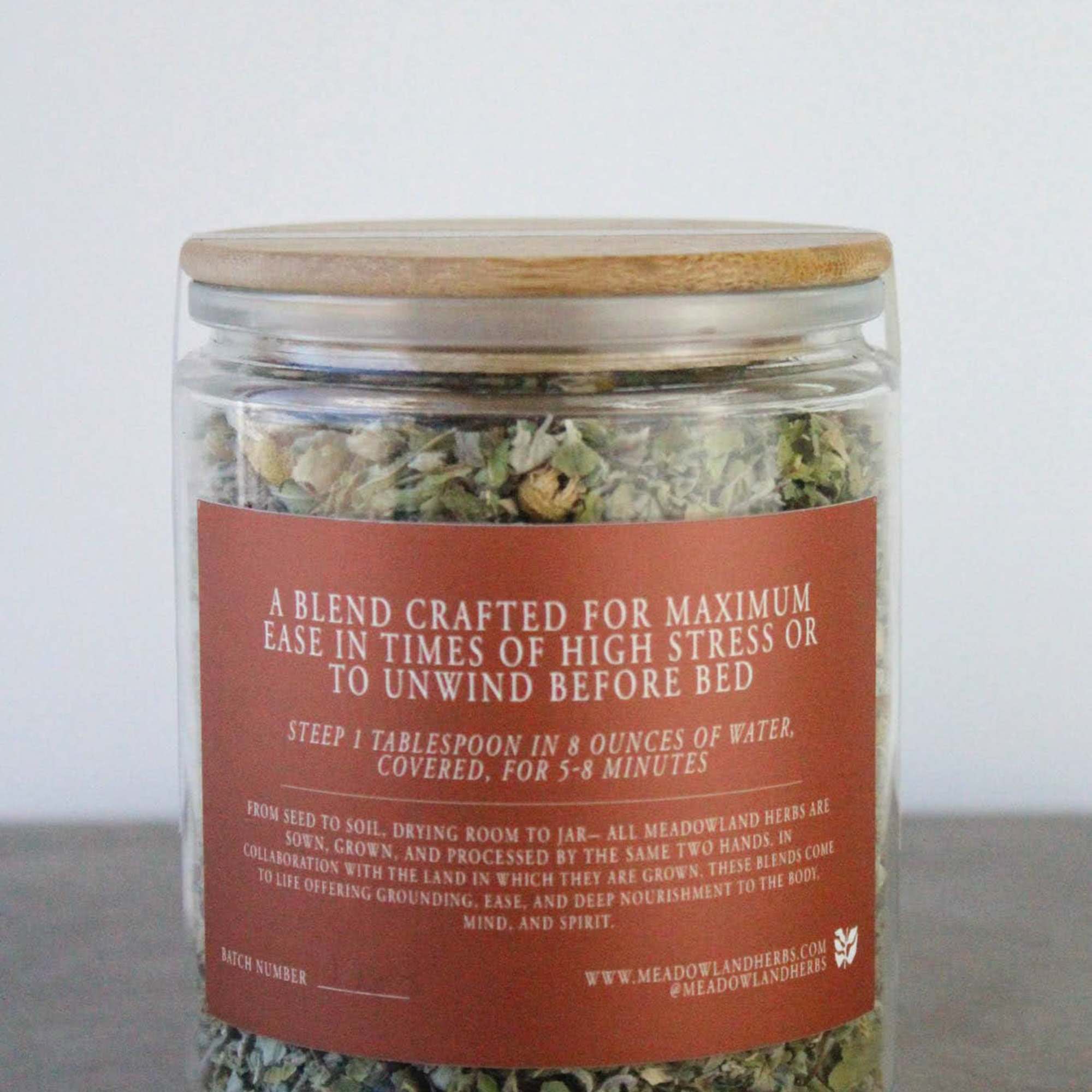 Glass jar of dried herbal tea blend with a wooden lid and red label