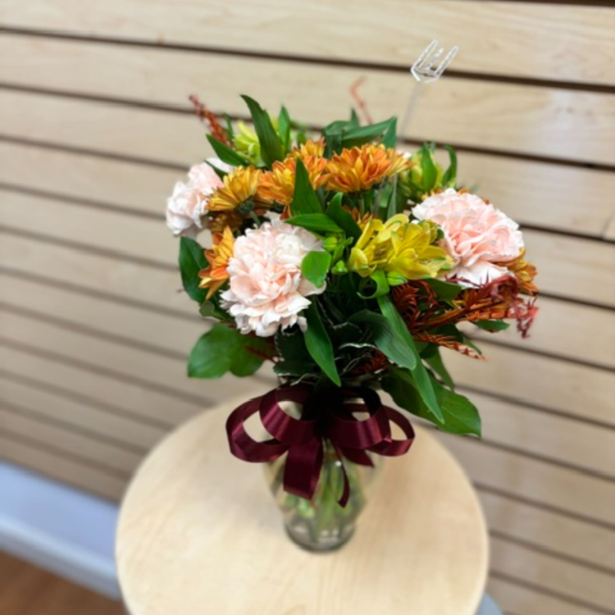 Bouquet of peach carnations and orange flowers in a glass vase with a ribbon