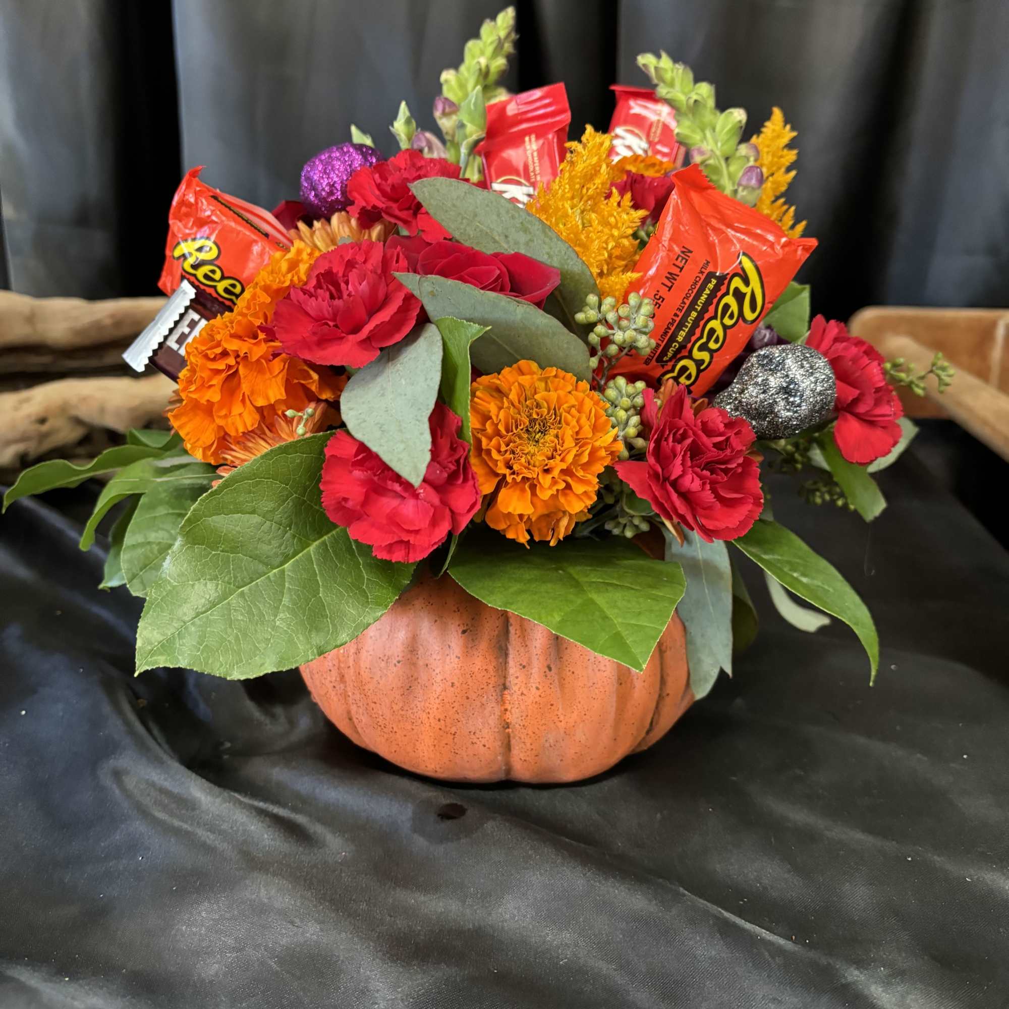 Bouquet in a pumpkin container with red and orange flowers and candy bars