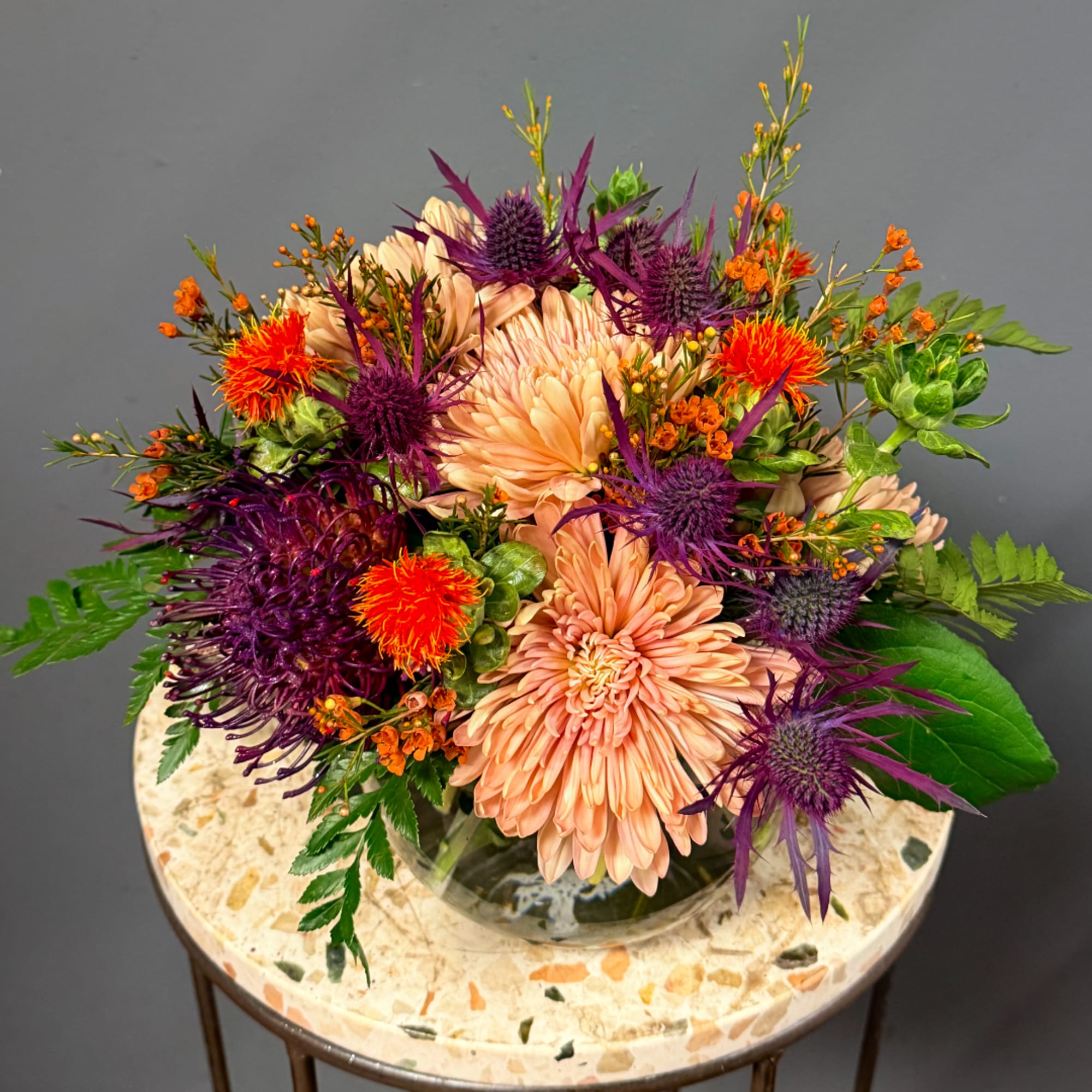 Peach and purple floral arrangement in a clear glass vase on a round table