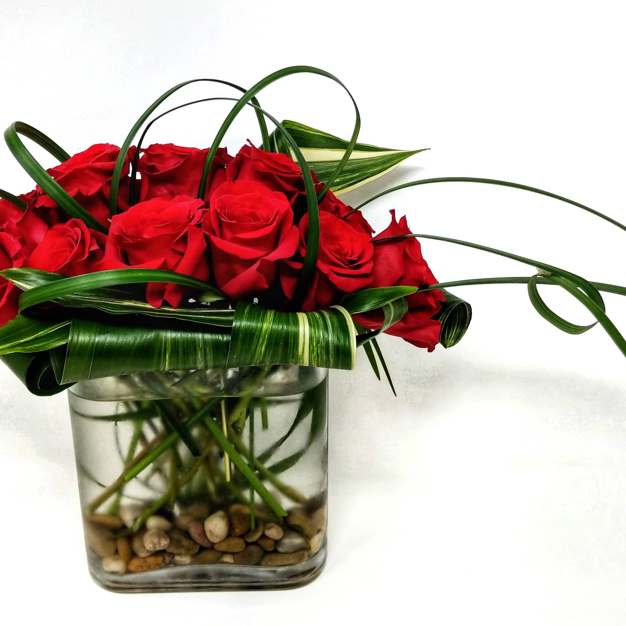 Red roses arranged in a square glass vase with looping green leaves