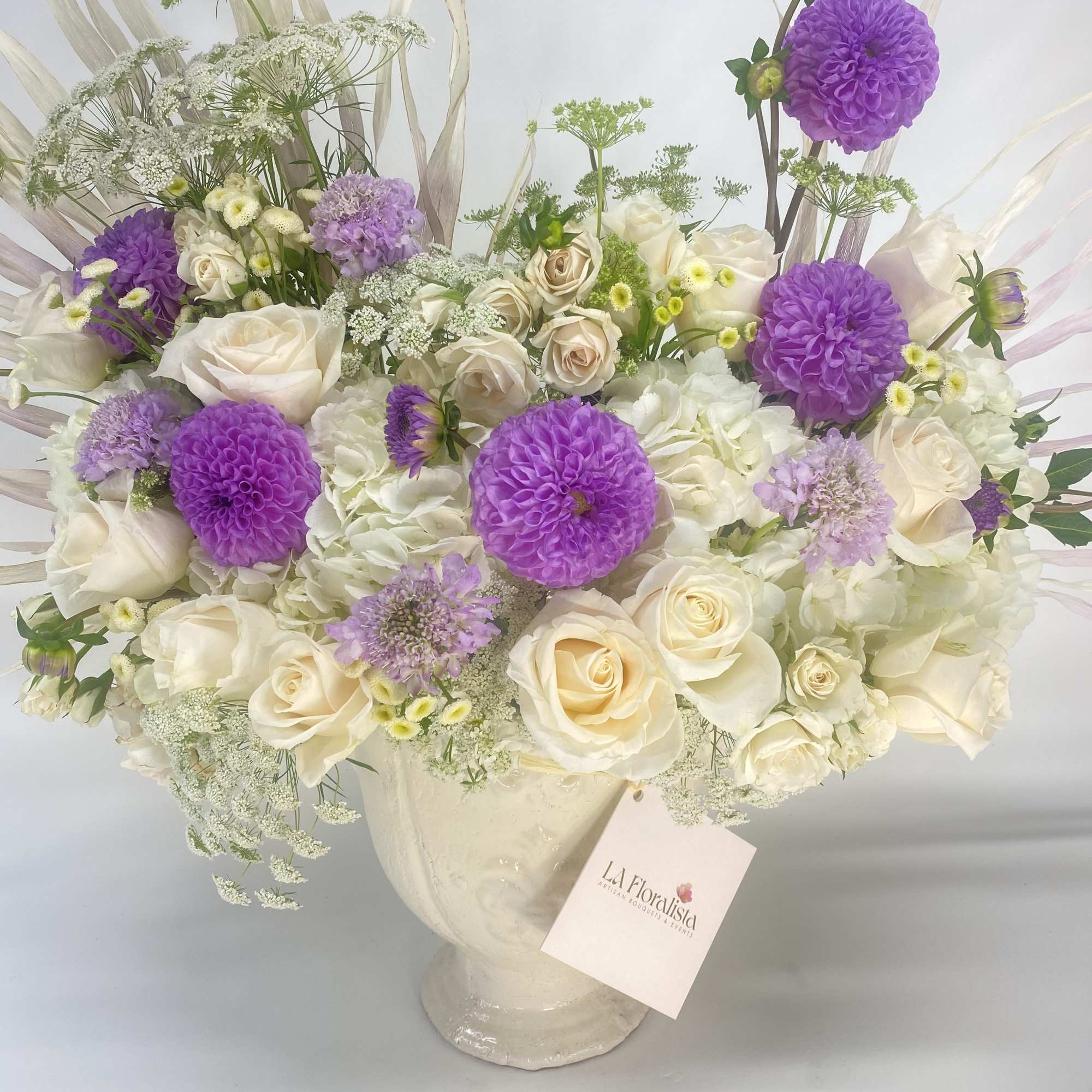 Bouquet of white roses and purple dahlias in a cream vase