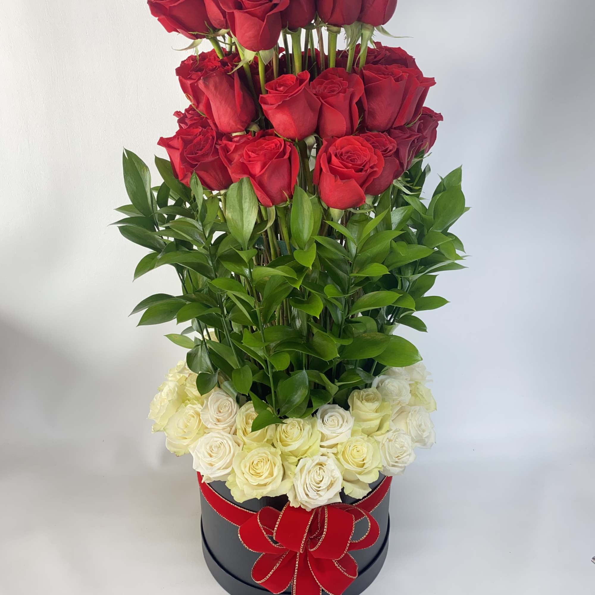 Tall arrangement of red and white roses in a black box with a red ribbon