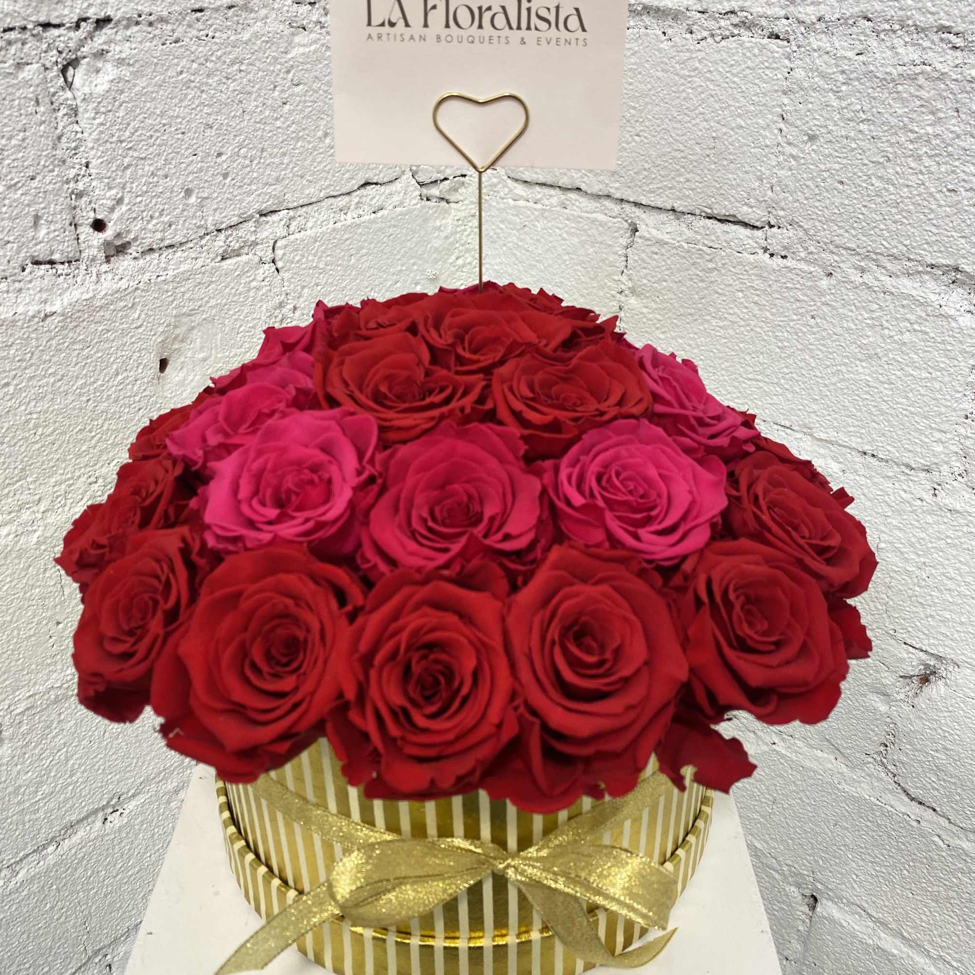 Round box of red and pink roses with a gold ribbon and card holder
