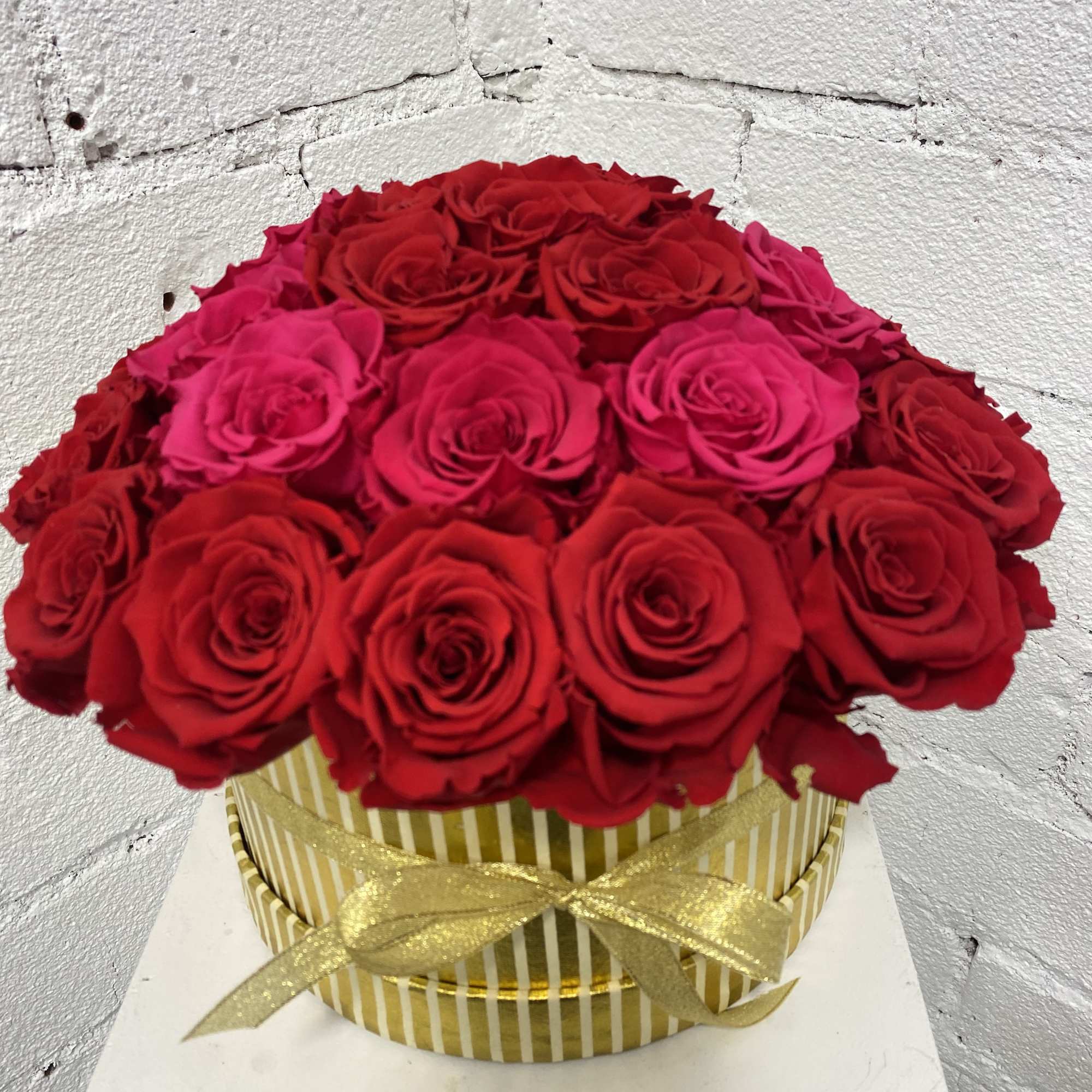 Round bouquet of red roses in a striped gold box with a ribbon