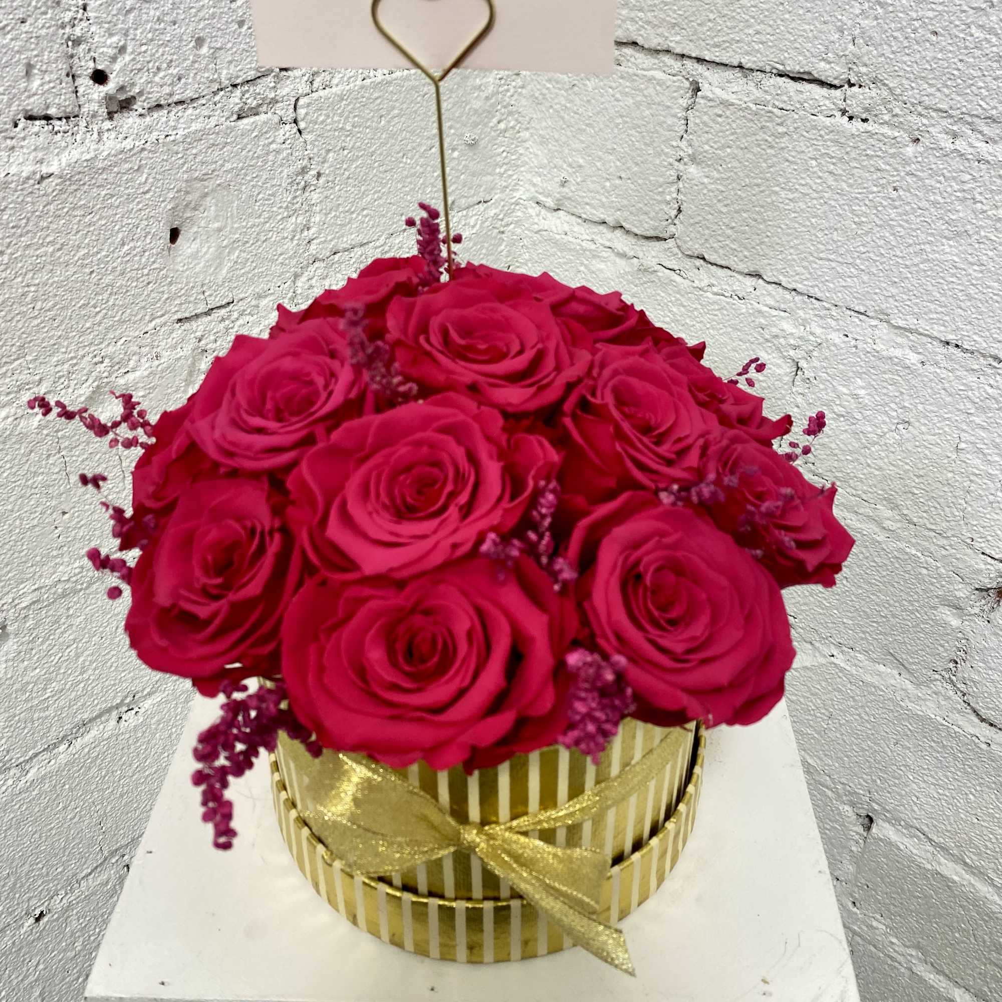 Round box arrangement of hot pink roses with a gold ribbon