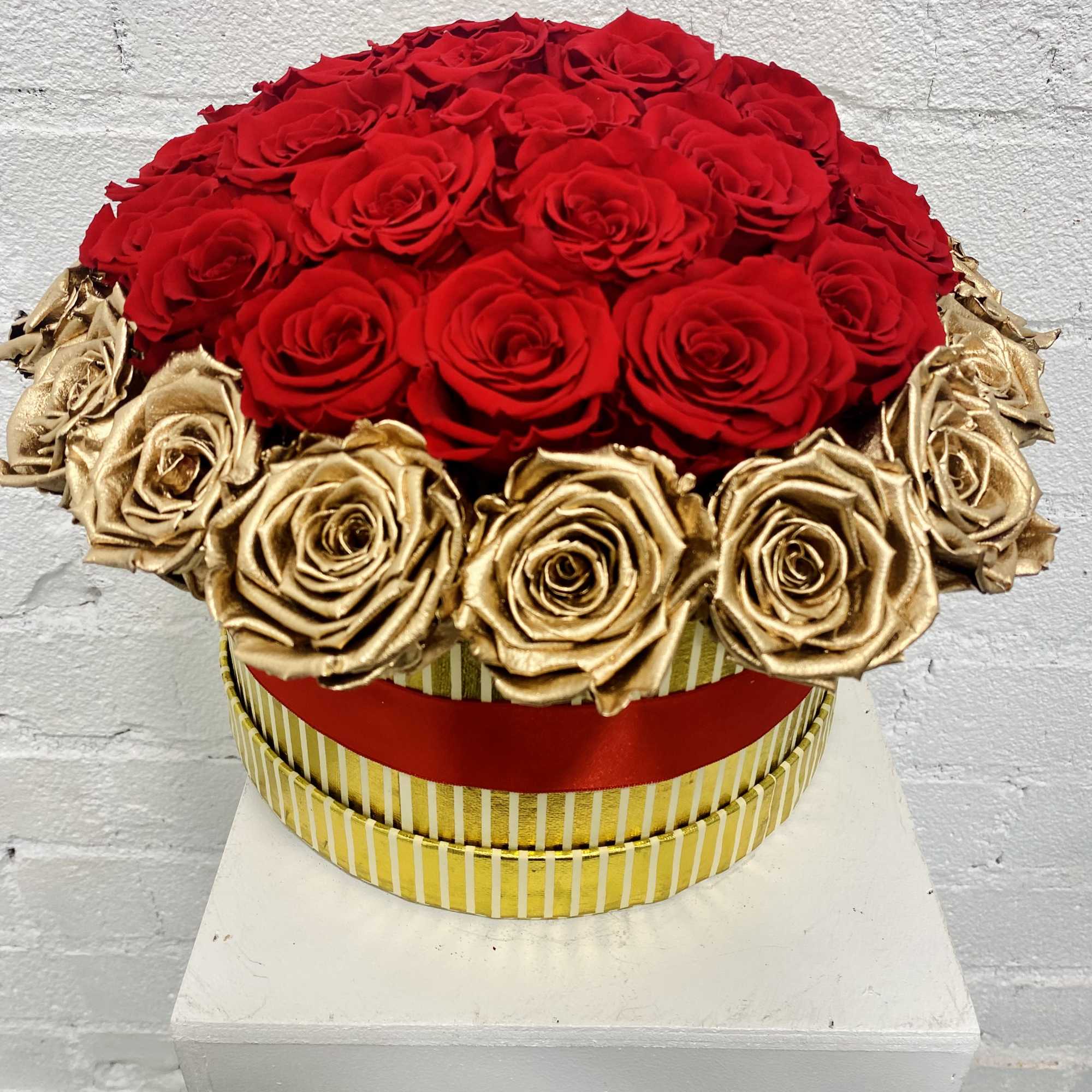 Round arrangement of red and gold roses in a striped box