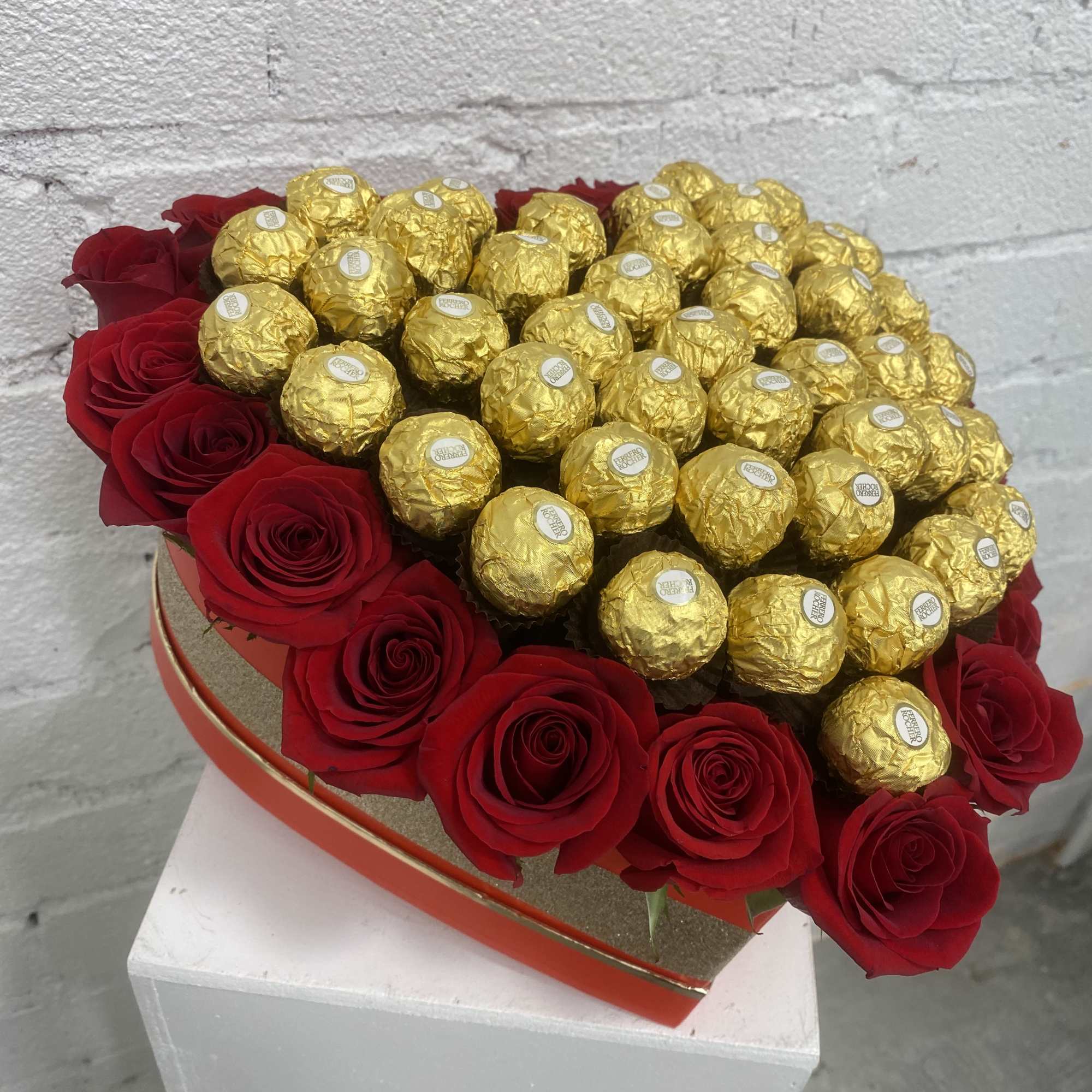 Heart-shaped box of red roses topped with gold-wrapped chocolates