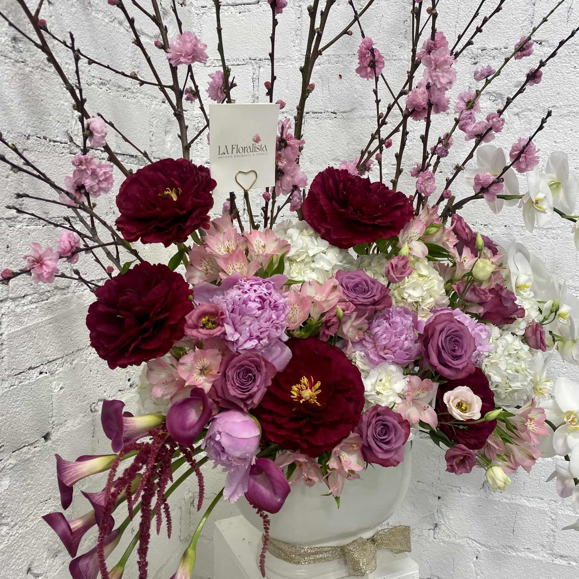 Large floral arrangement in a white vase with pink and burgundy blooms