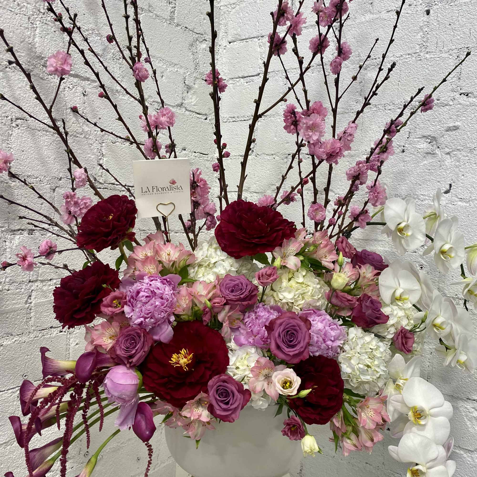 Large floral arrangement in a white vase with pink, red, and white blooms