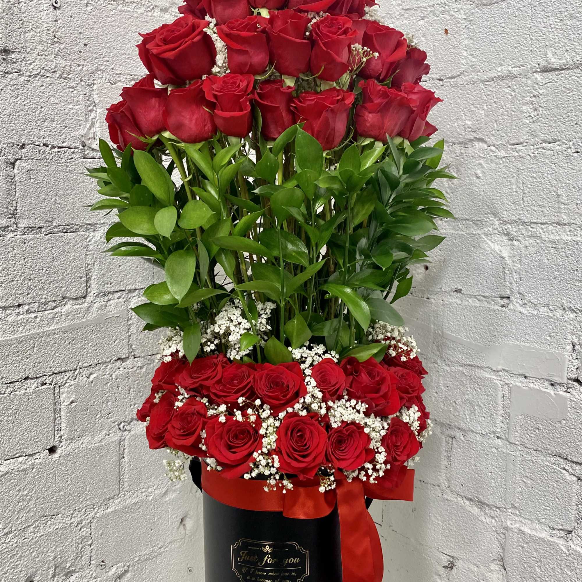 Tall arrangement of red roses in a black box with a red ribbon