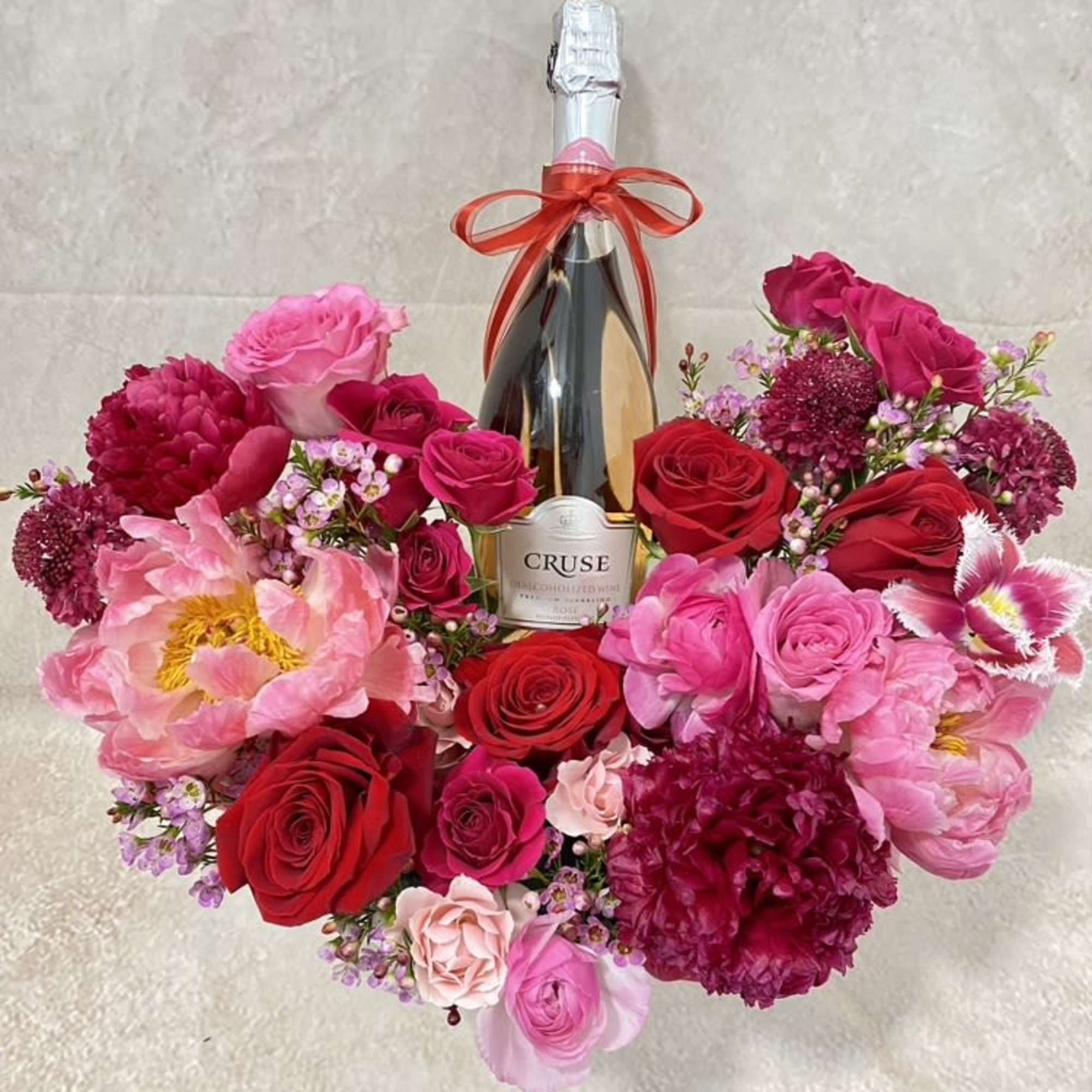 Heart-shaped bouquet of pink and red flowers around a champagne bottle