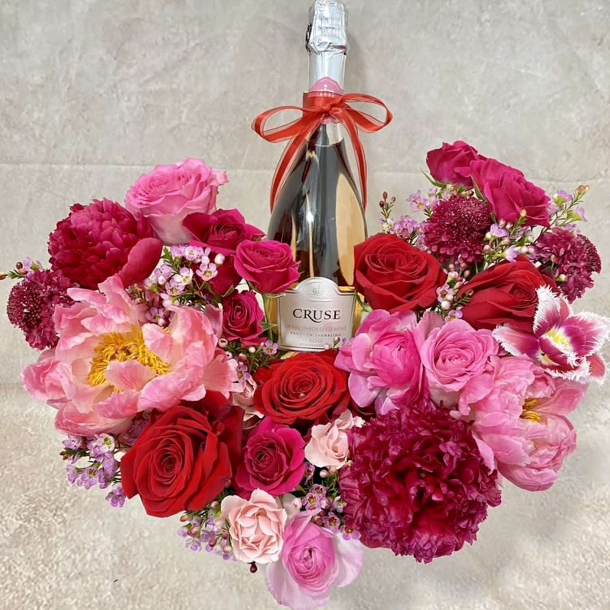 Heart-shaped bouquet of pink and red flowers around a champagne bottle, photo 2 of 2