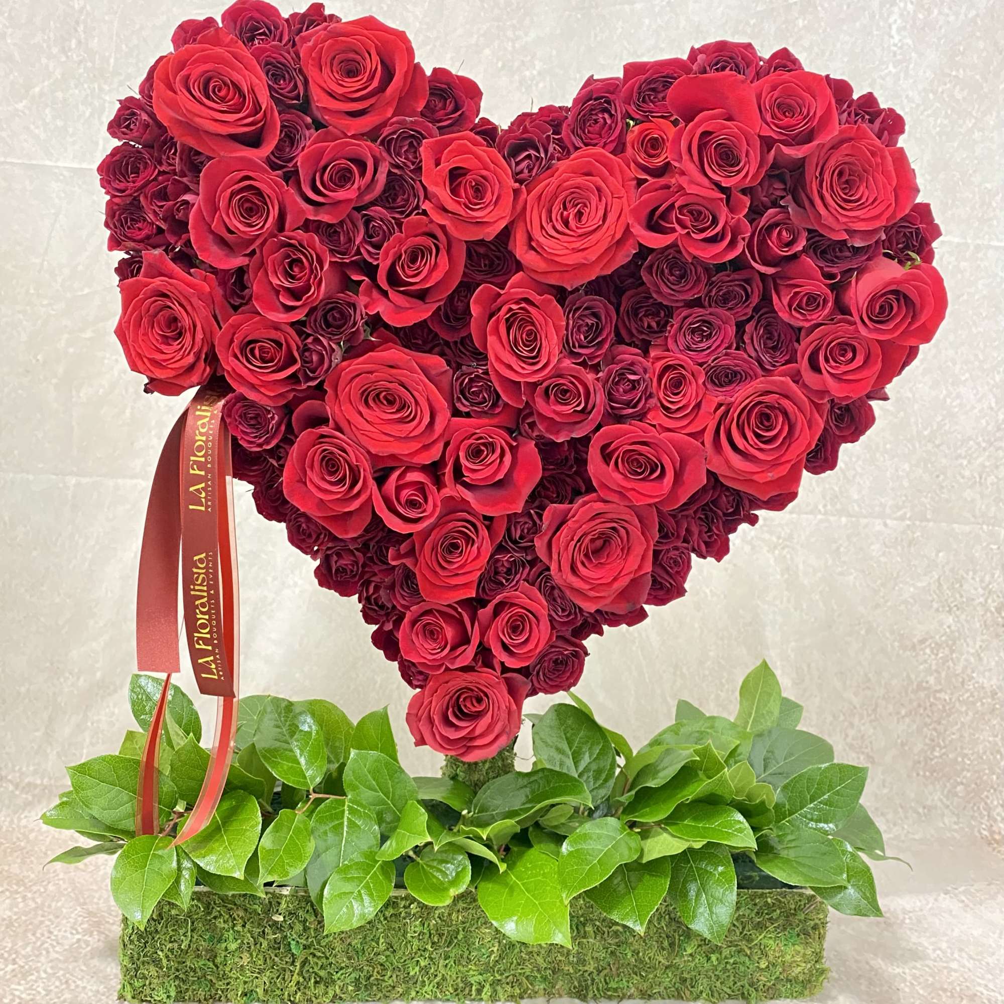 Heart-shaped arrangement of red roses on a moss base with green leaves