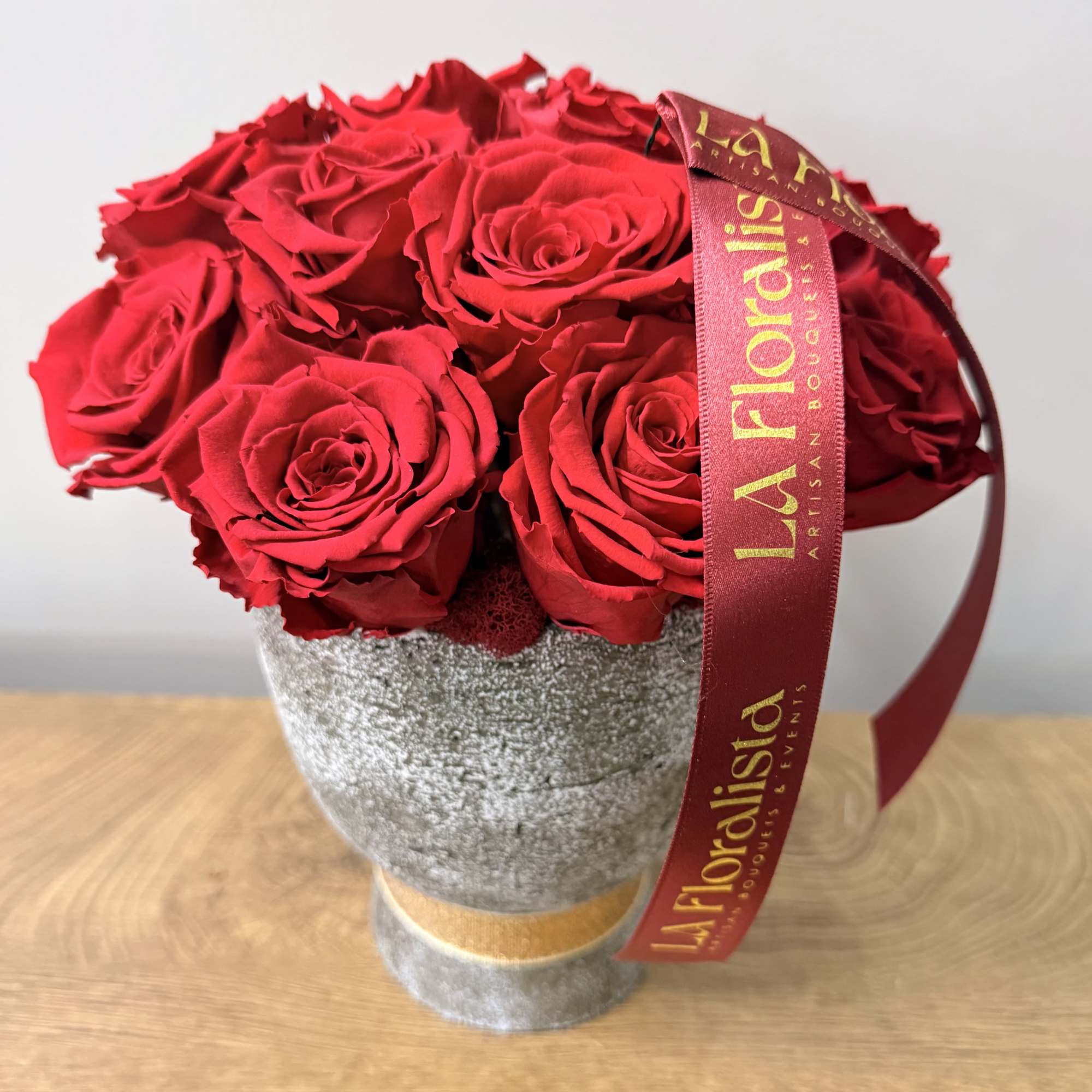 Red roses arranged in a gray textured vase with a ribbon