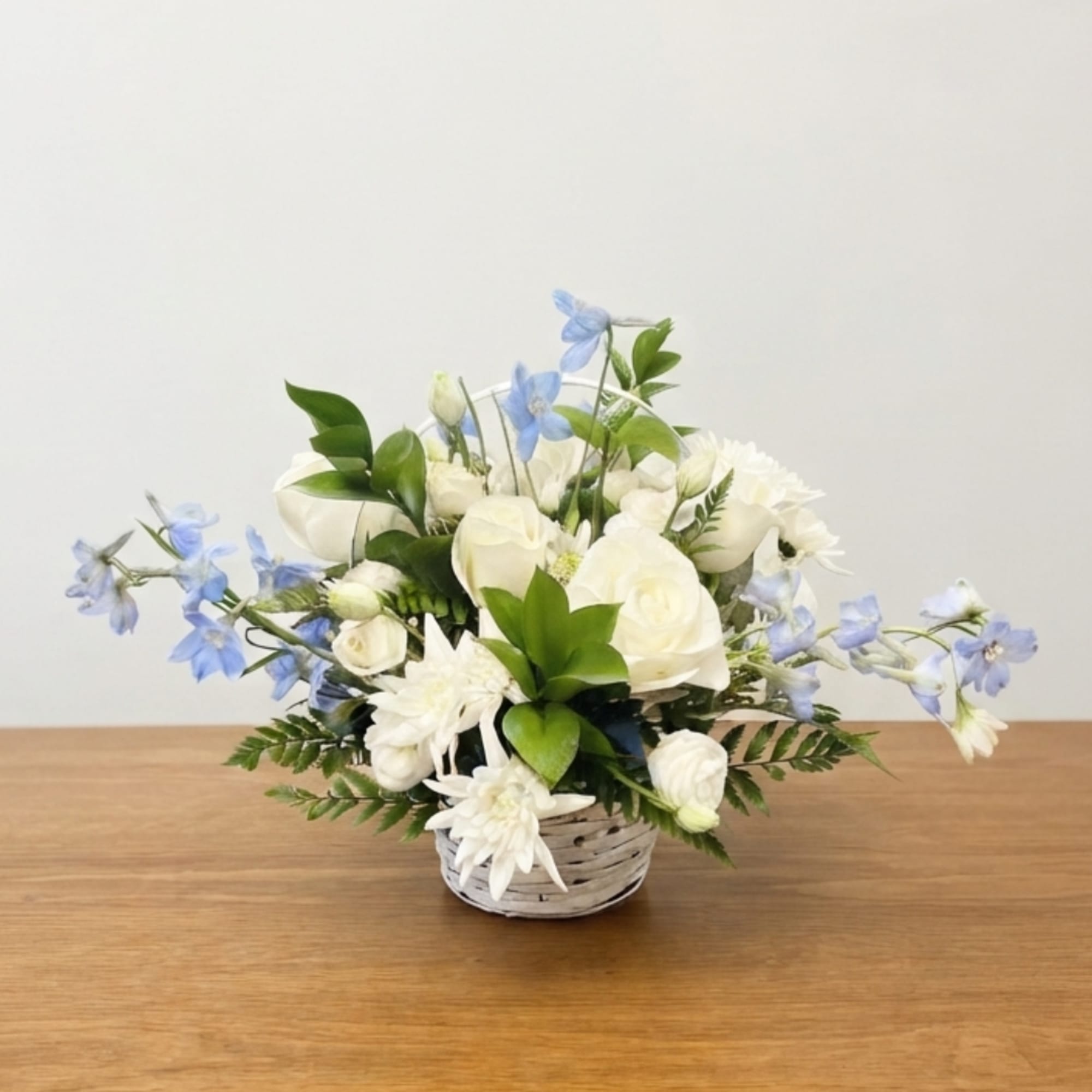 White roses and blue flowers arranged in a small wicker basket
