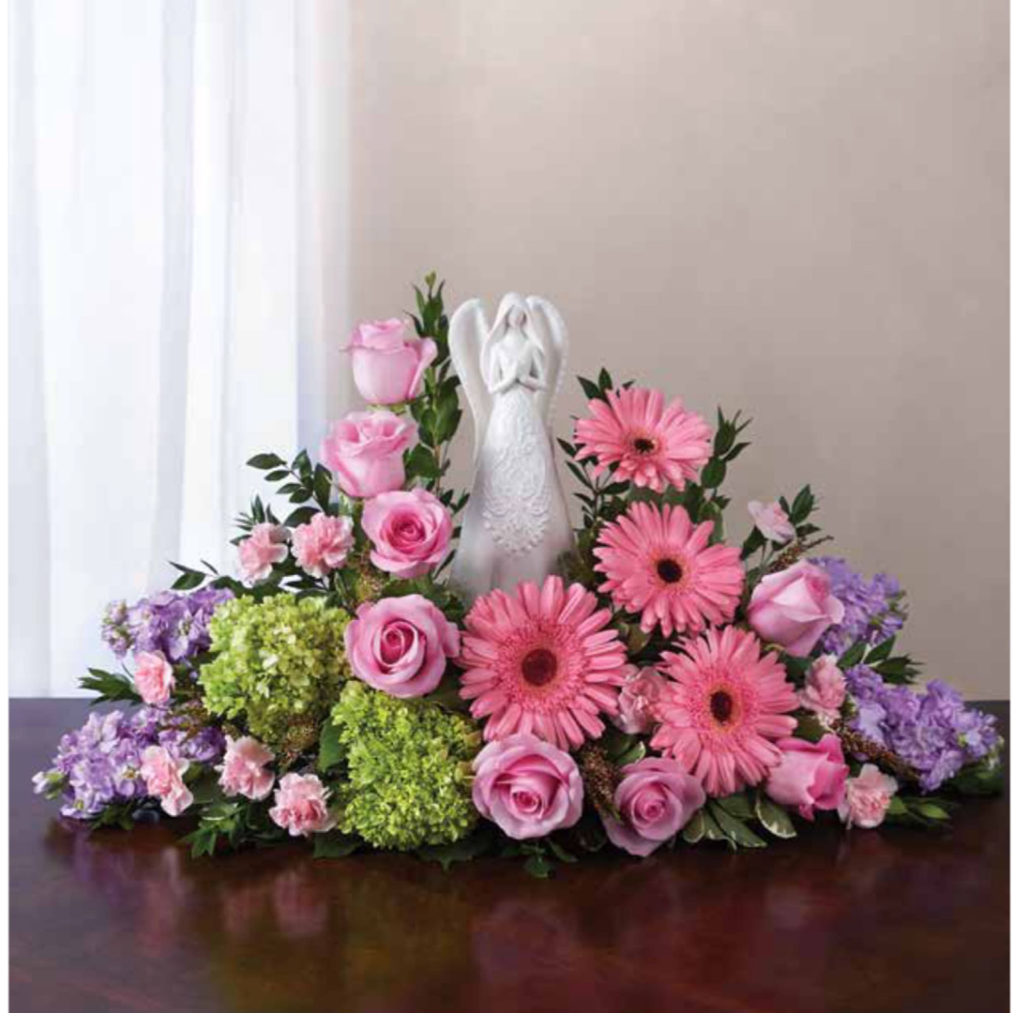 Pink and purple floral arrangement with a white angel figurine in the center
