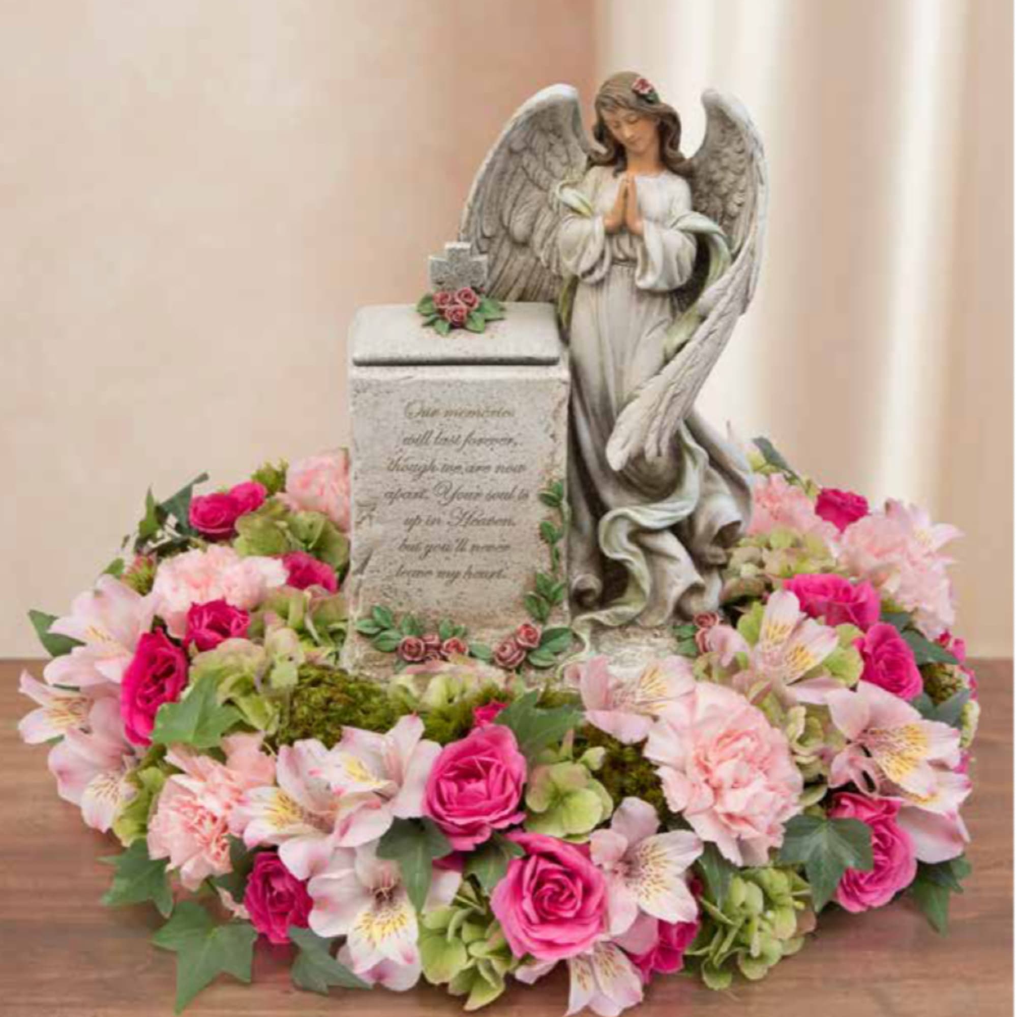 Pink and white floral wreath around an angel statue and memorial stone