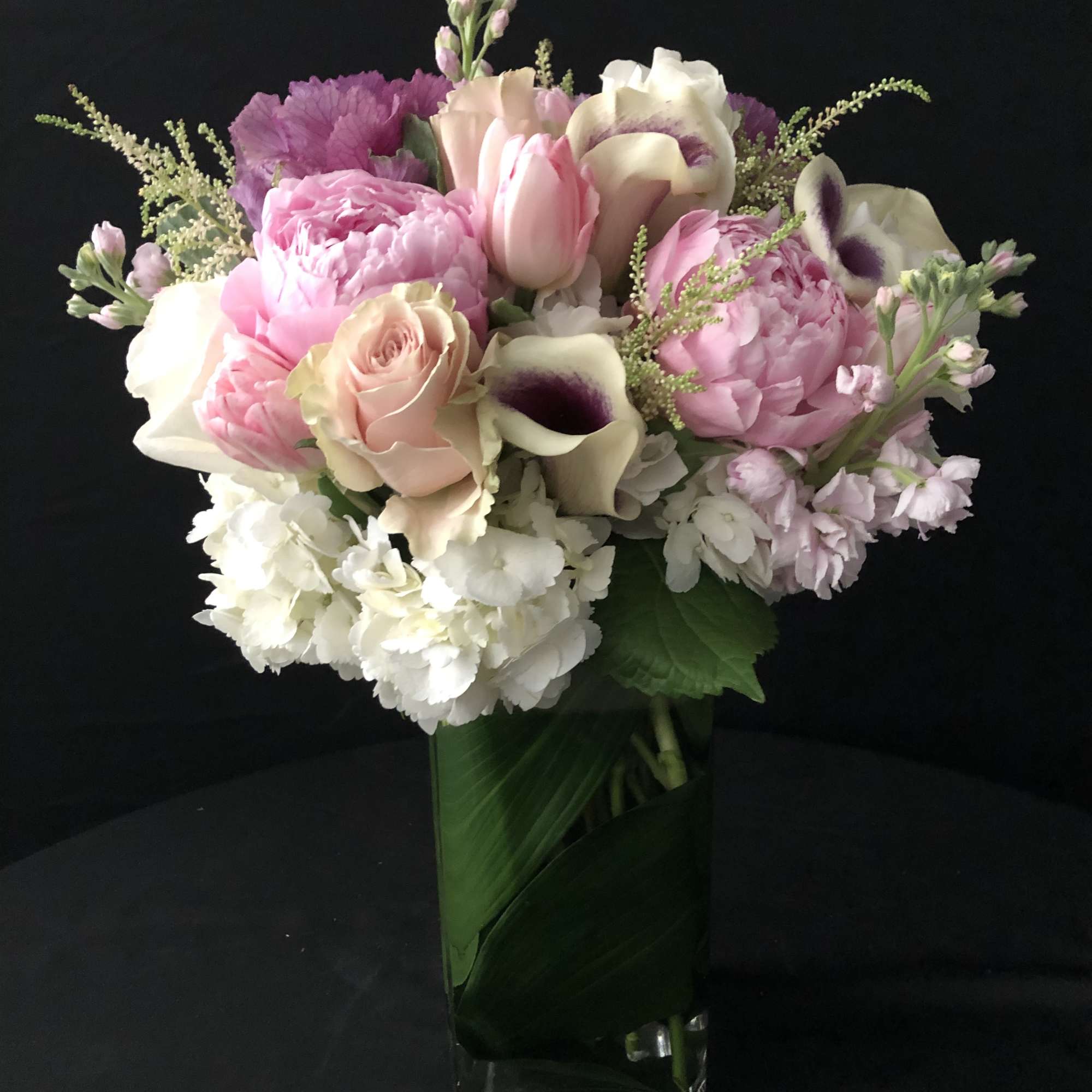 Tall arrangement of pink and white flowers in a clear glass vase lined with green leaves.