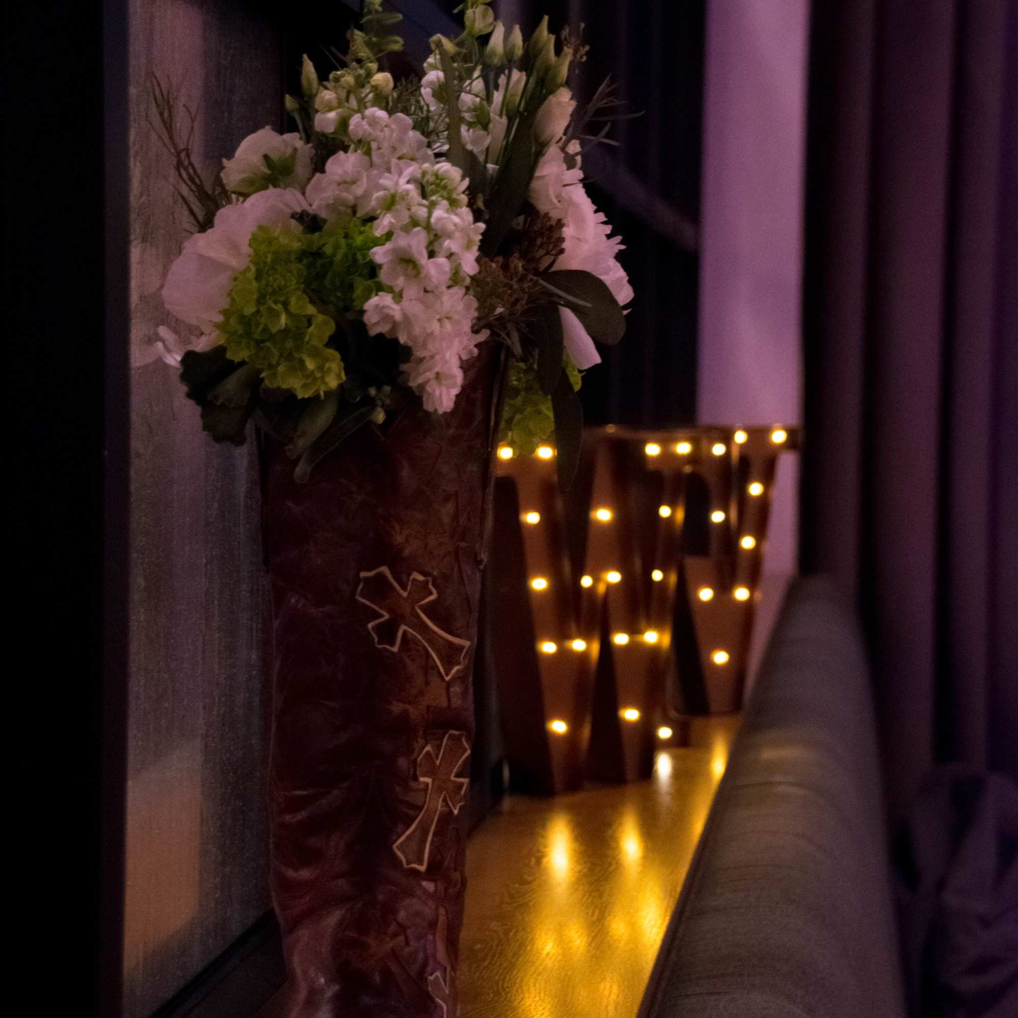 Tall floral arrangement in a burgundy boot-shaped container with white and green blooms.